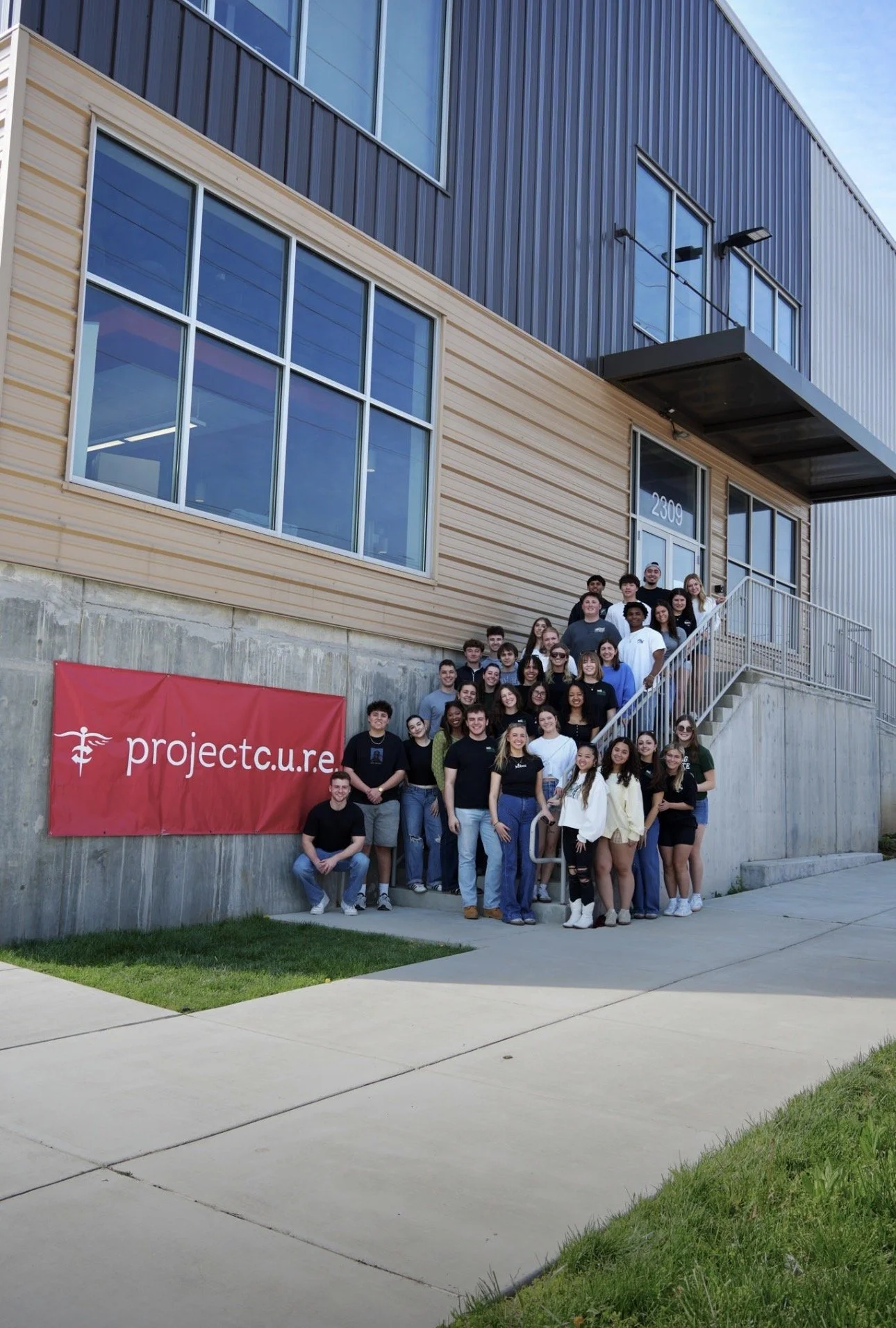 Group of smiling young people standing together in a room with a presentation screen behind them displaying statistics about food donations.