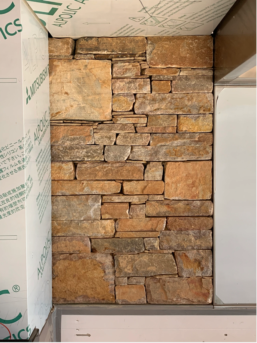 Natural stone wall with stacked stones, surrounded by sheets of building material labeled with brand logos and text.