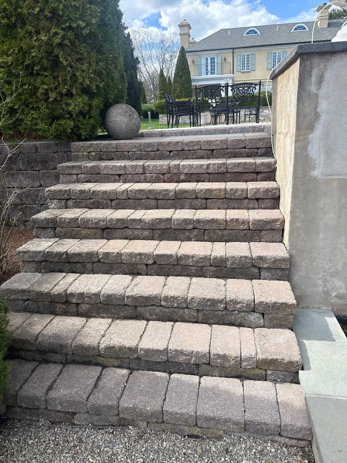 Stone block steps flanked by stacked stone retaining walls at an Atlantic Highlands, NJ home, leading up to a patio on graded terrain.