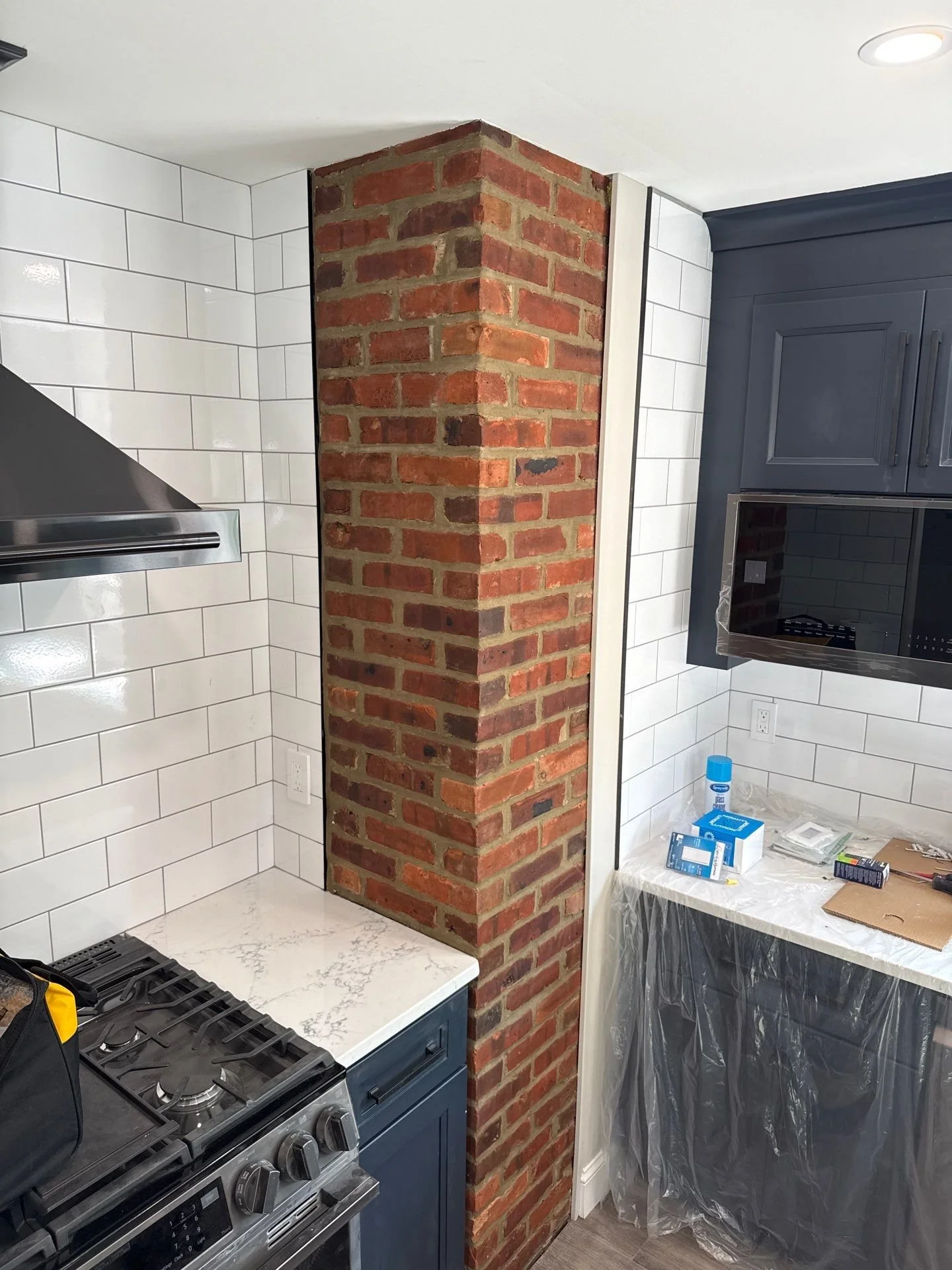 Exposed interior brick chimney column in an Atlantic Highlands, NJ kitchen featuring original red brick set against white subway tile.