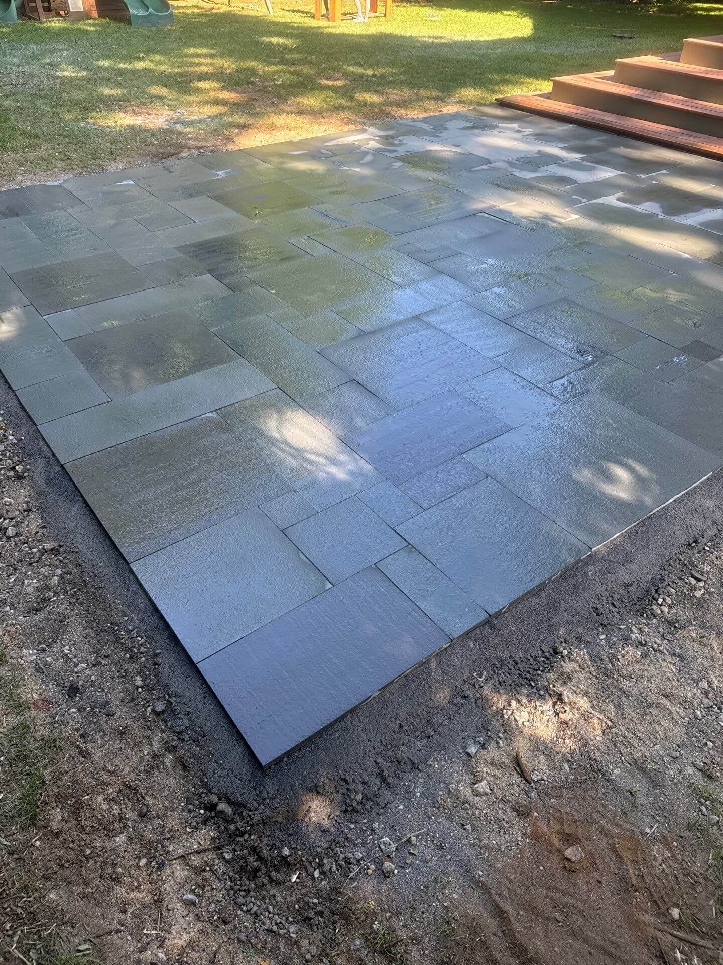 Bluestone patio laid in a random rectangular pattern in a backyard, meeting a wood deck staircase at a Rumson, NJ home.