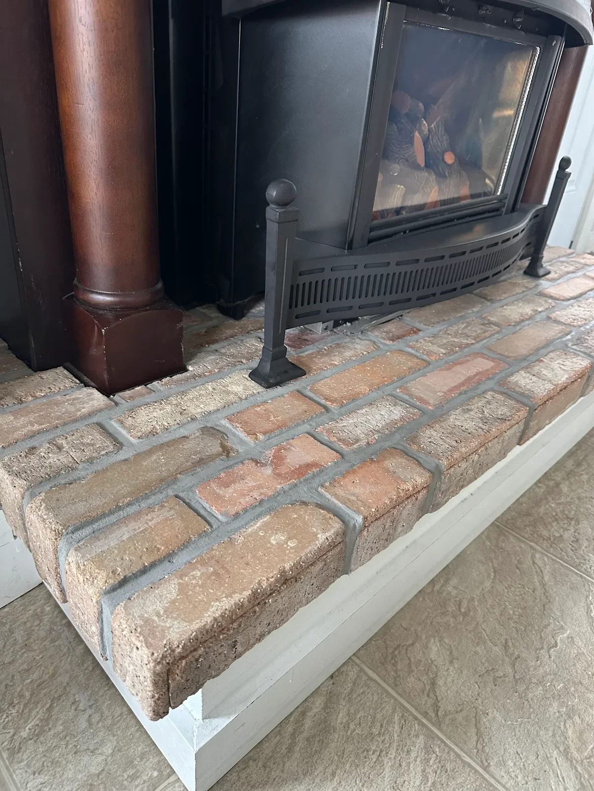 Raised brick hearth with fresh mortar joints in front of a black wood-burning fireplace insert and wood surround at a Red Bank, NJ home.