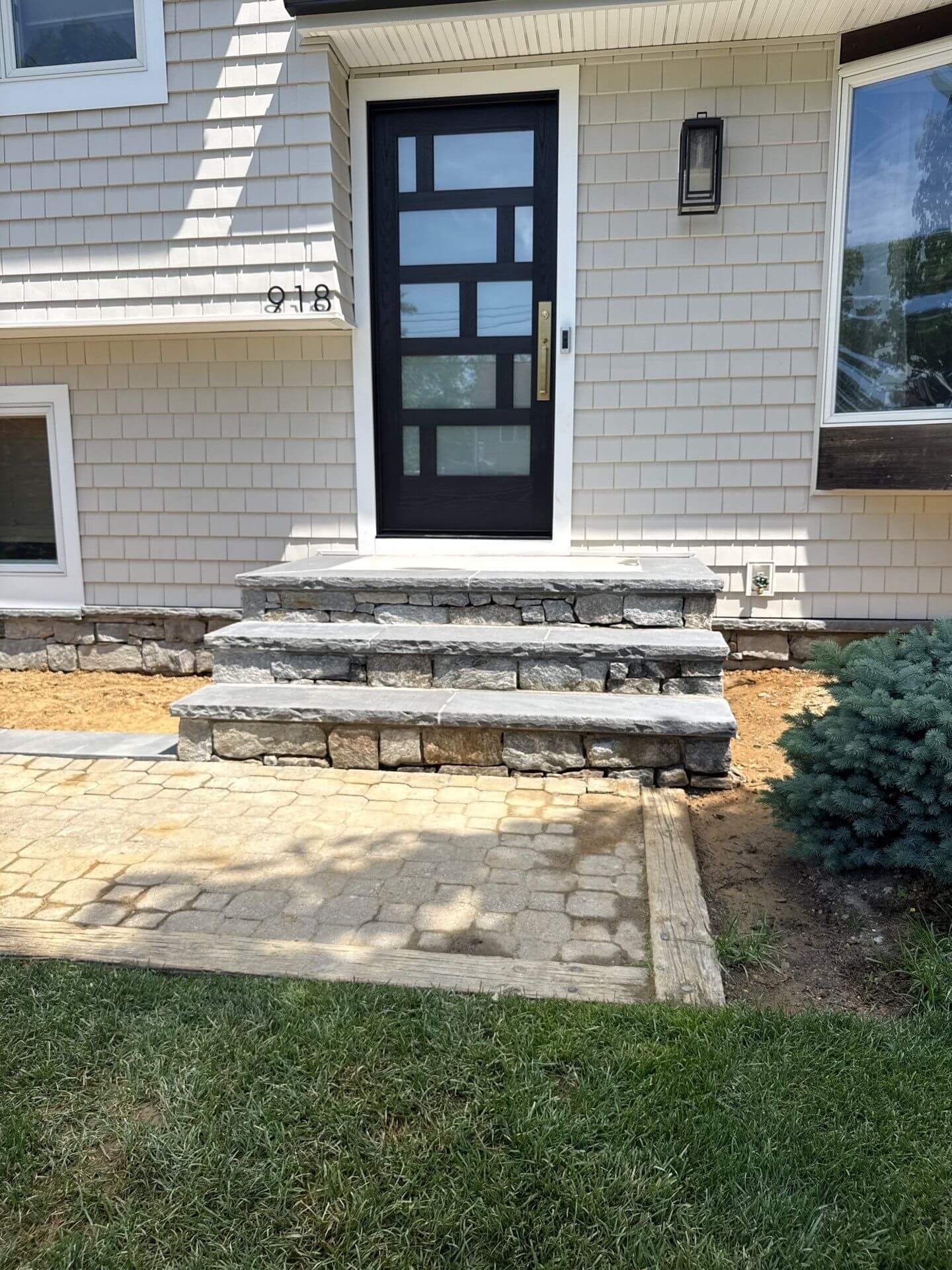 Natural stone front steps with bluestone treads and a stacked stone base leading to a black front door, paired with a cobblestone paver walkway at a Monmouth County, NJ home.