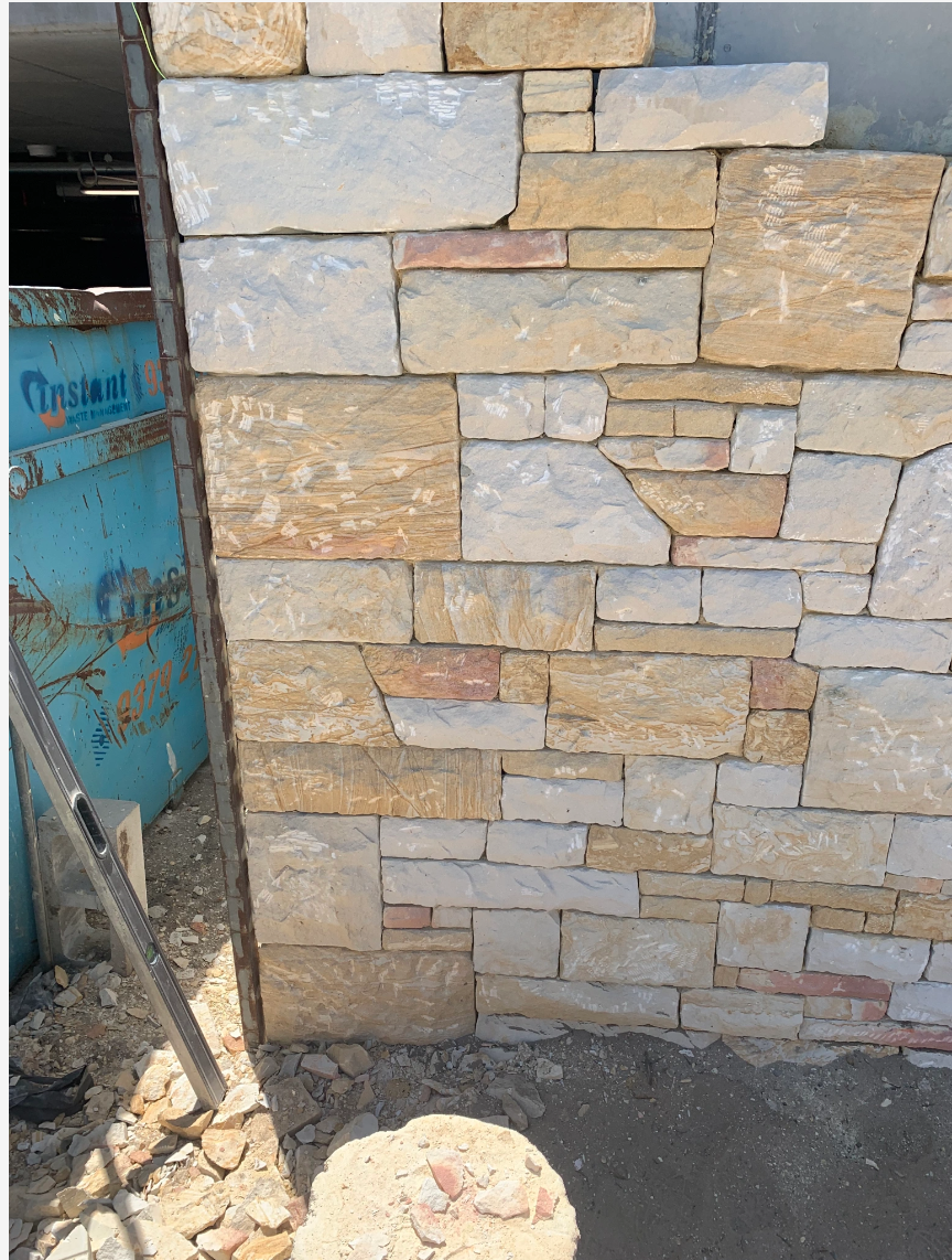 Close-up of a stone wall with rough, irregularly shaped bricks in earthy tones, adjacent to a blue metal container and a construction level leaning against the wall.