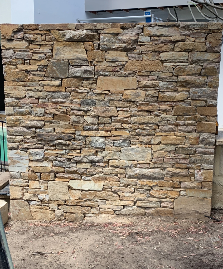 Stacked stone wall with rustic appearance made from irregular, unevenly sized stones in various earth tones.