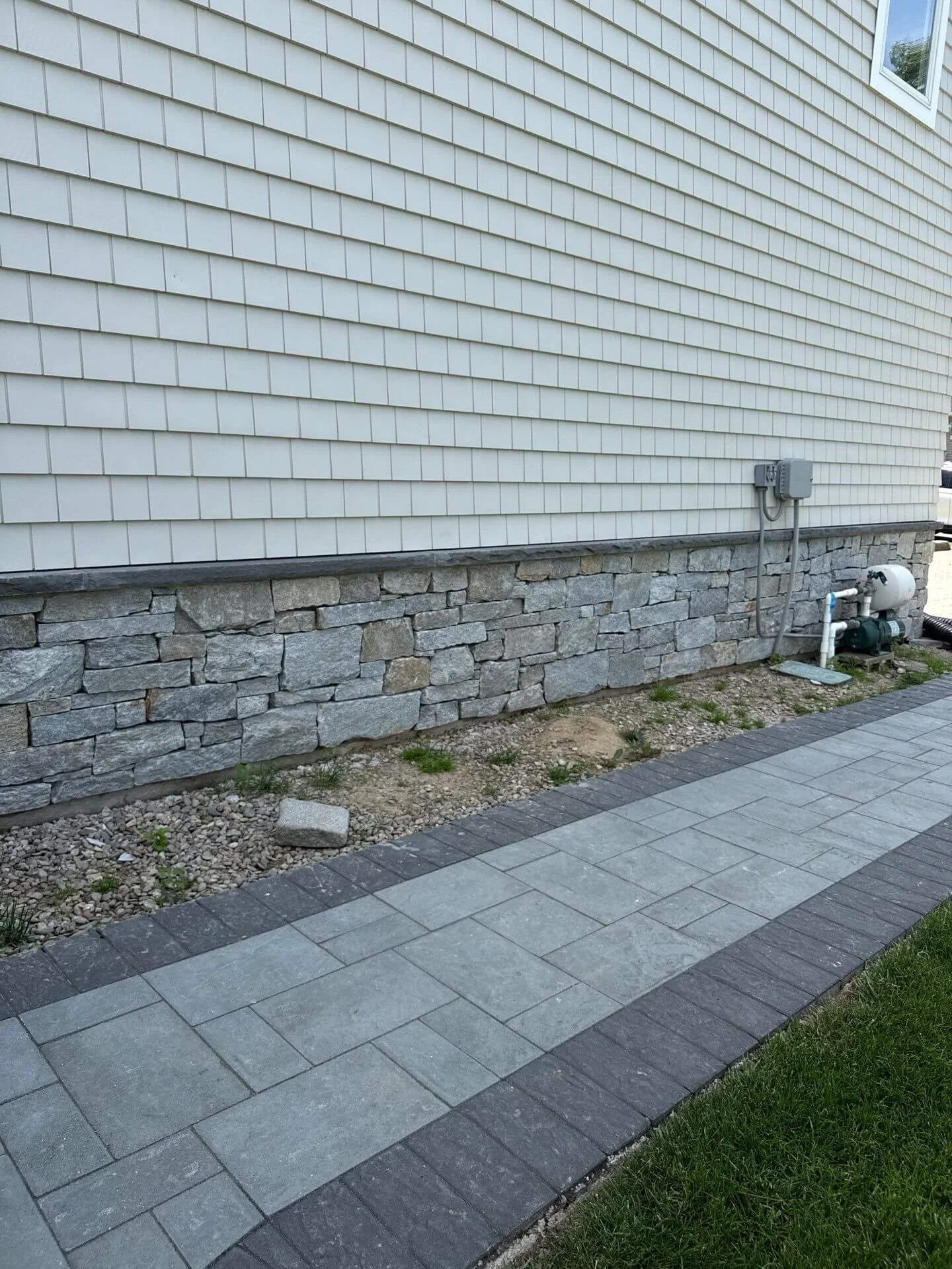 Gray stone veneer foundation wall with a bluestone cap running alongside a paver walkway with a dark border at a Red Bank, NJ home.