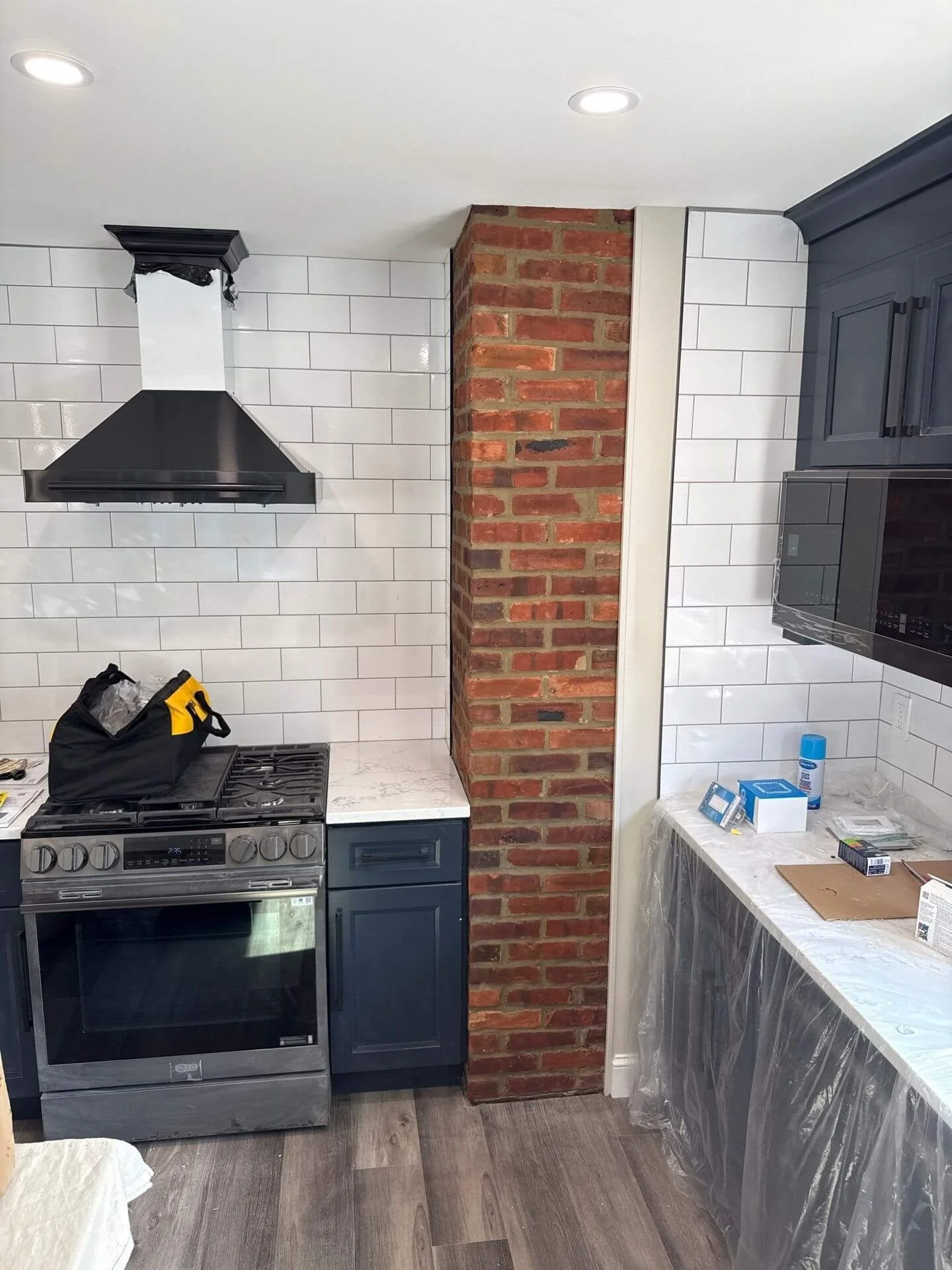 Exposed red brick chimney column with restored mortar joints between white subway tile walls in a kitchen at a Red Bank, NJ home.