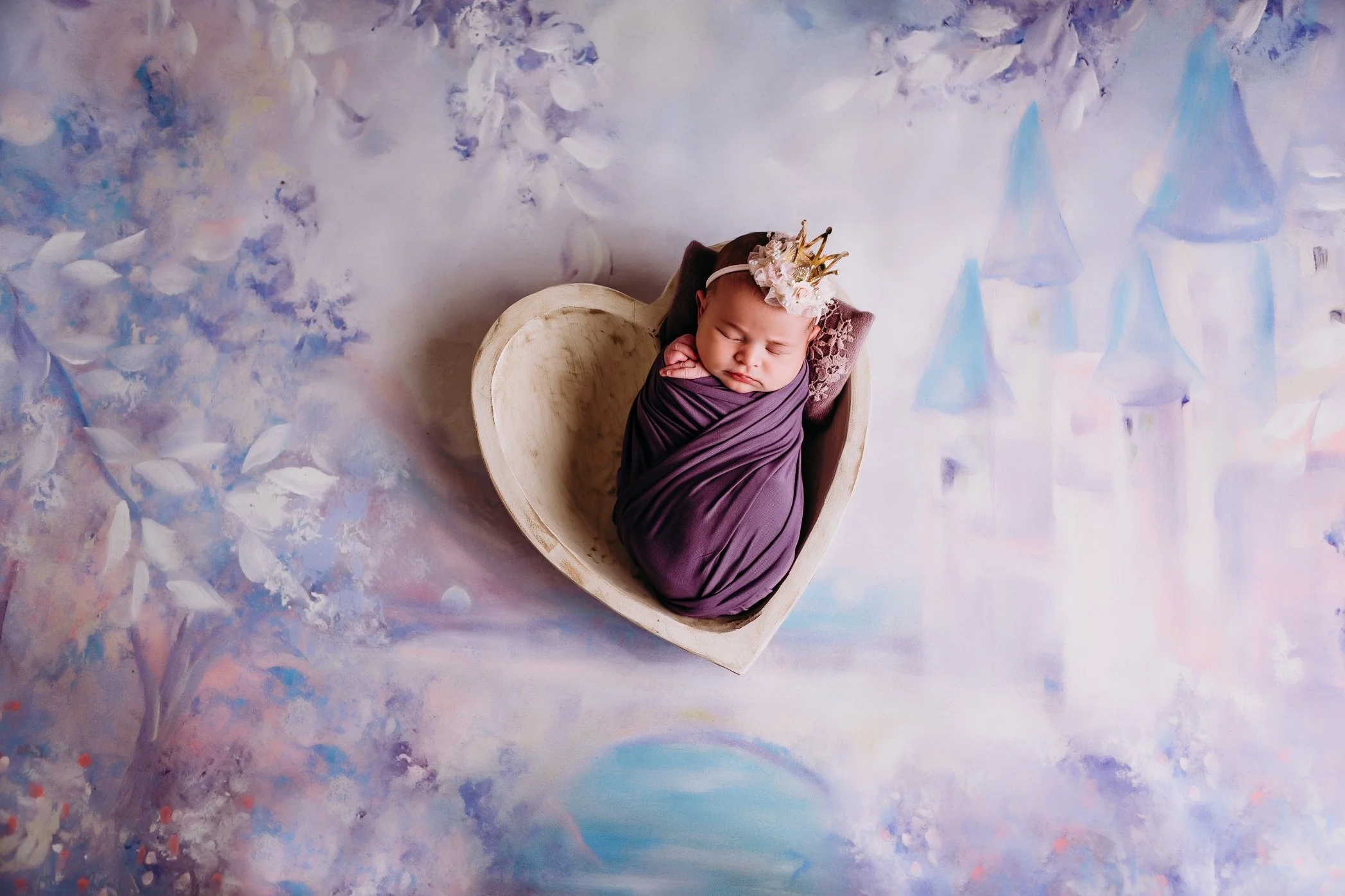 A baby wrapped in a purple wrap in a heart bowl.