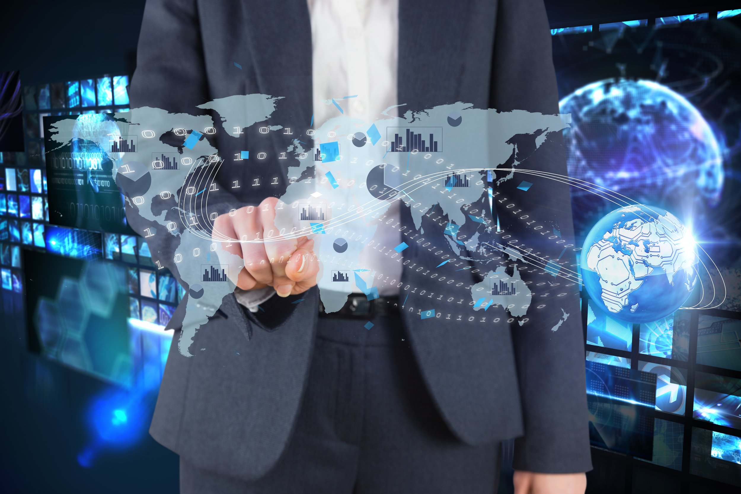 Person in business attire pointing at a transparent digital map of the world overlaid with graphs and binary code, with a background of digital screens and global icons.