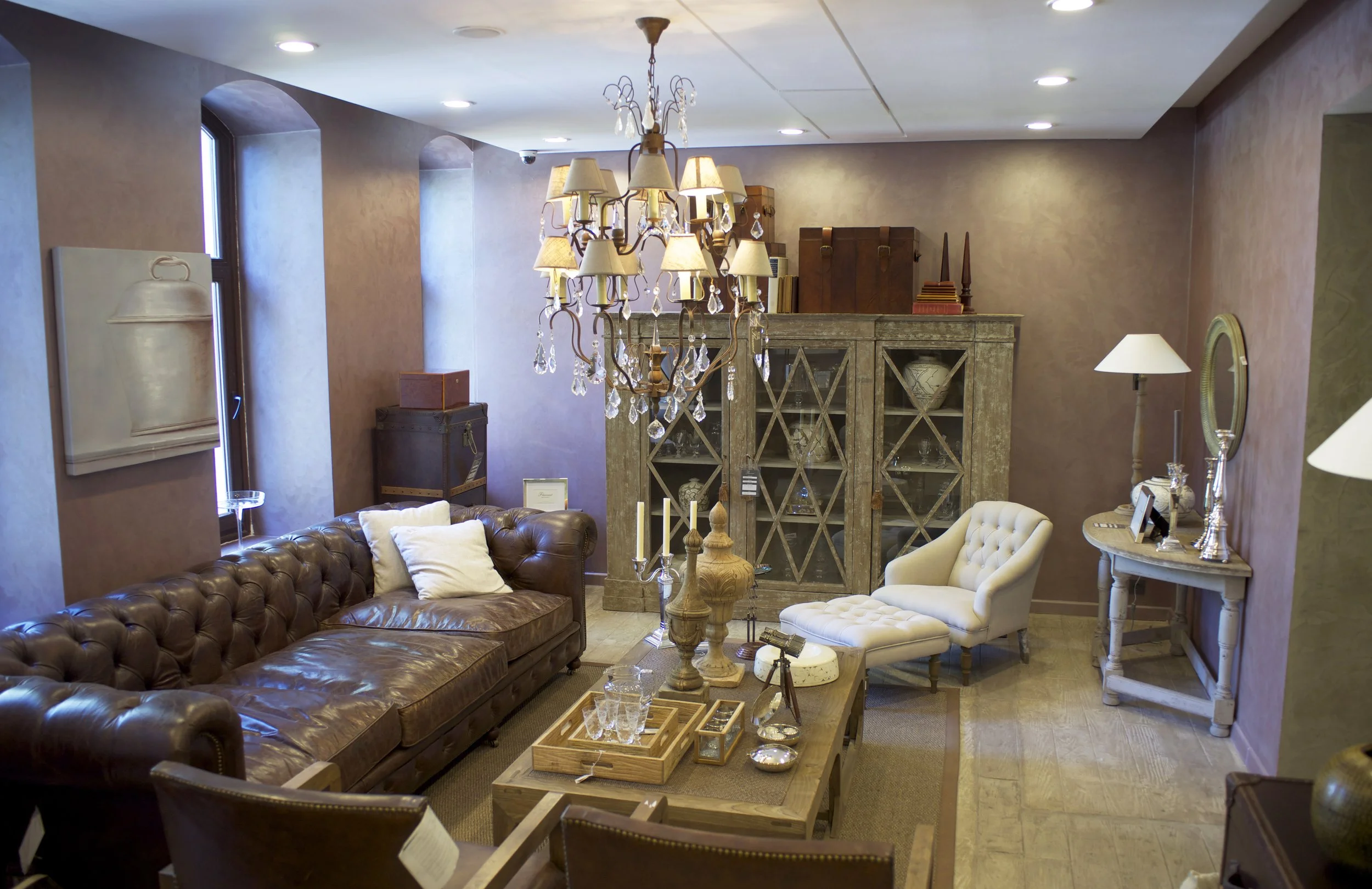 Interior of a cozy living room with leather and fabric armchairs, a wooden coffee table, and a chandelier hanging from the ceiling, along with various lamps and decorative items.