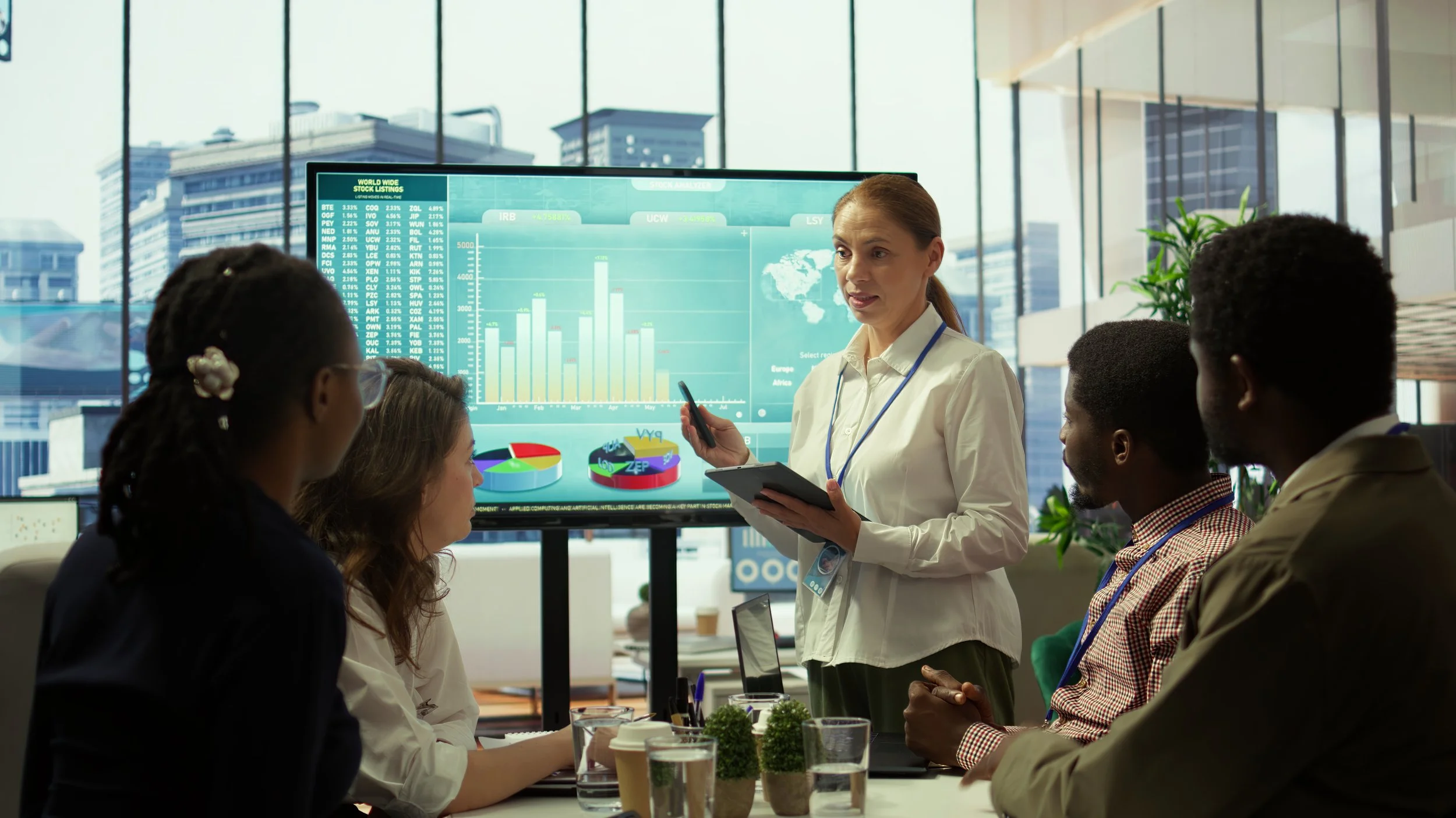 Businesswoman giving presentation to a diverse group in an office with large windows, showing financial charts on a screen.