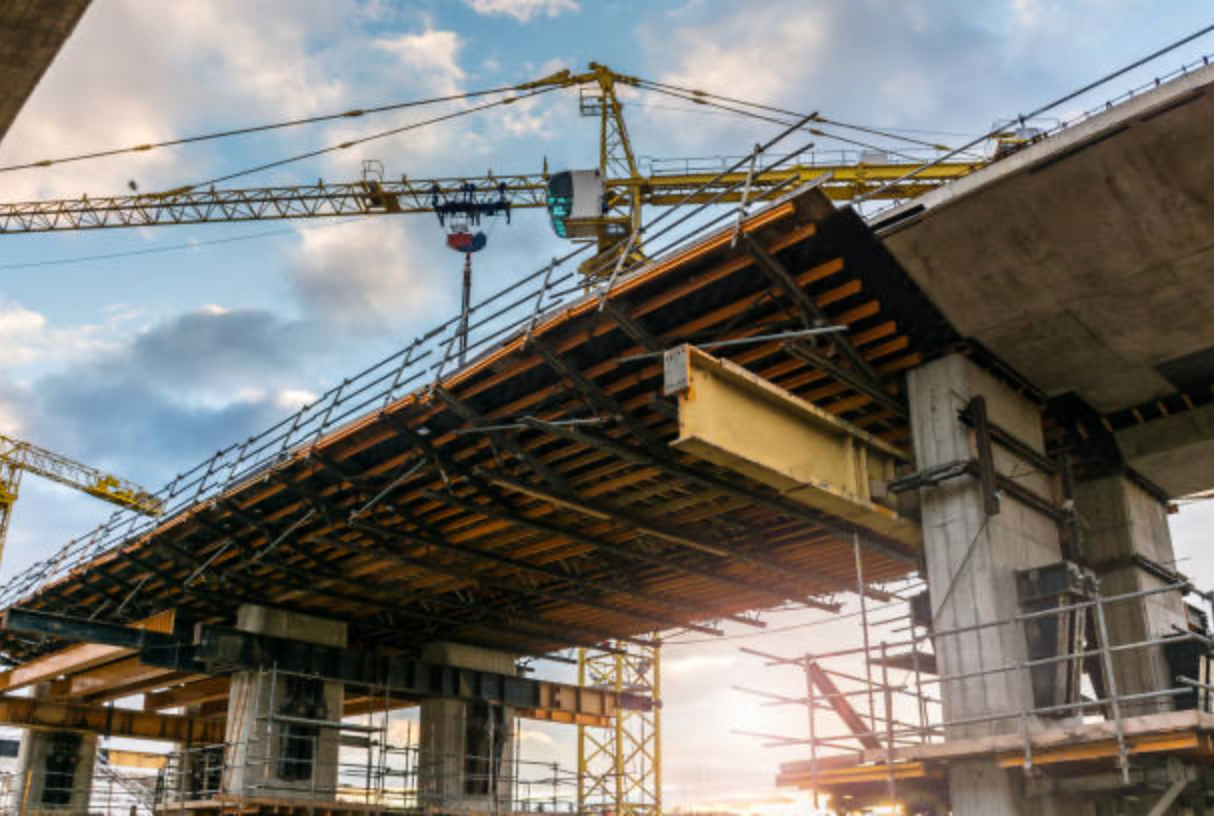 Under construction bridge with cranes and scaffolding at sunset.