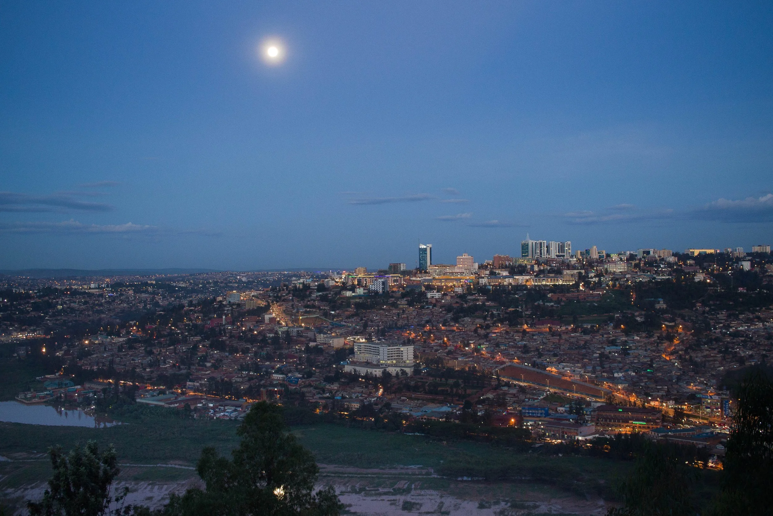 Nighttime city skyline with high-rise buildings and a full moon in the sky.