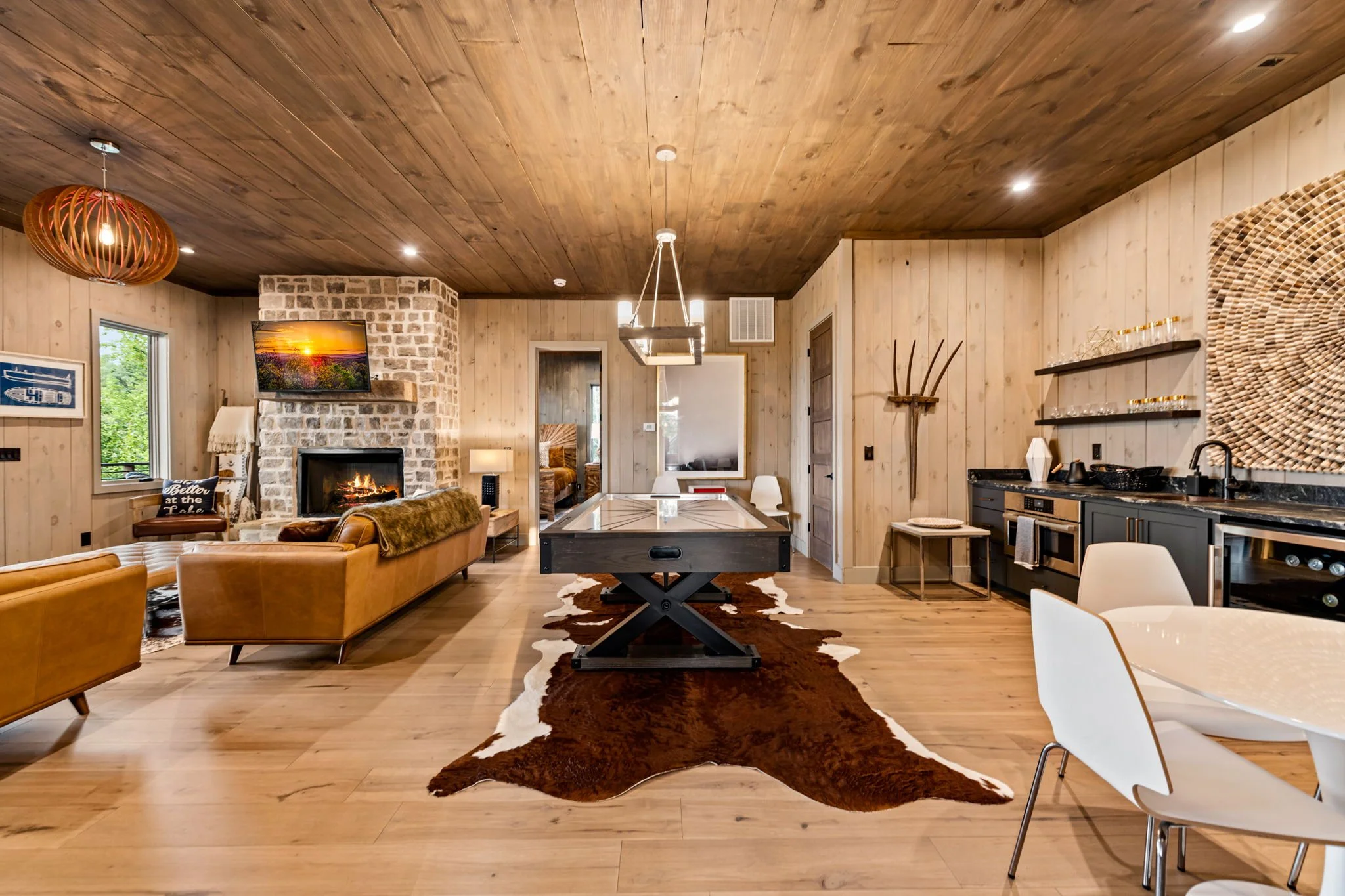 Entertain in this stylish lounge featuring a shuffleboard table, wet bar with sink, beverage fridge, lounge seating, stone fireplace, and designer lighting—a spacious game and gathering area perfect for relaxing and socializing.