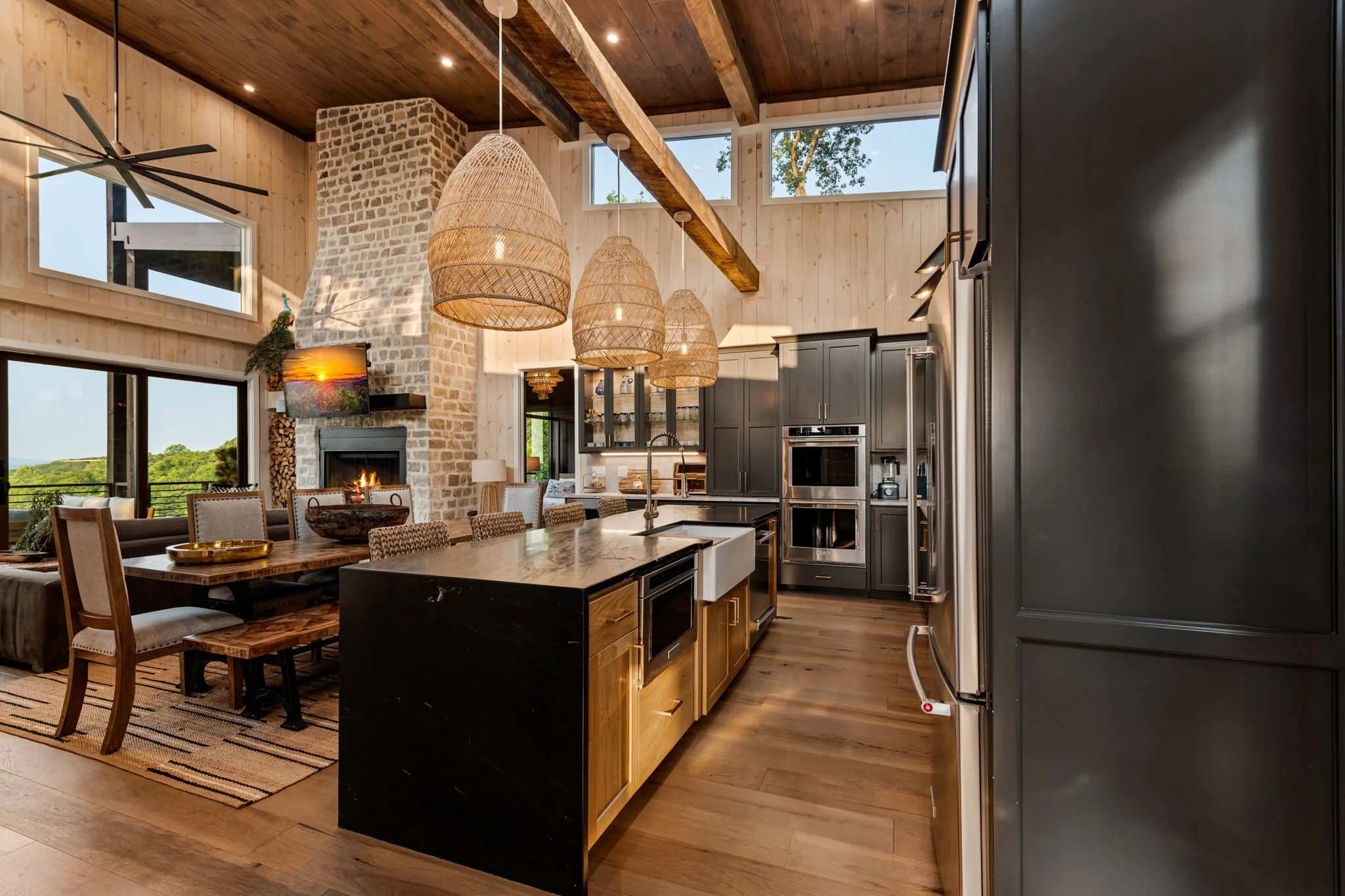 Cook & gather in this luxury open-concept kitchen featuring a large island with seating, stainless steel appliances, double ovens, custom cabinetry, designer pendant lighting, and seamless flow to dining & living areas w/ a stunning stone fireplace.