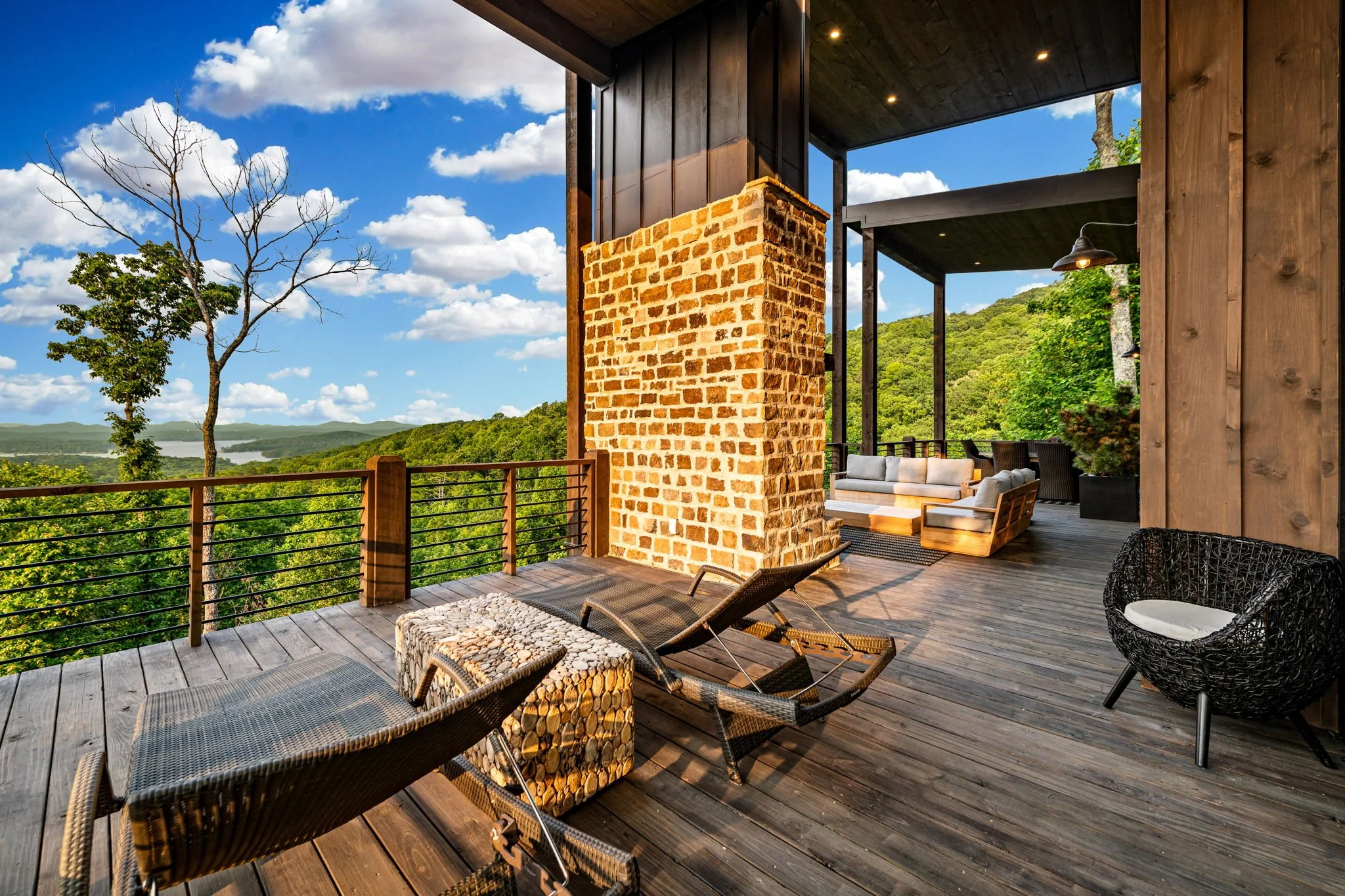 Relax on the expansive covered deck featuring chaise loungers, stylish outdoor seating, and panoramic mountain & lake views—a serene luxury space perfect for sunbathing, unwinding, or enjoying peaceful moments surrounded by nature.