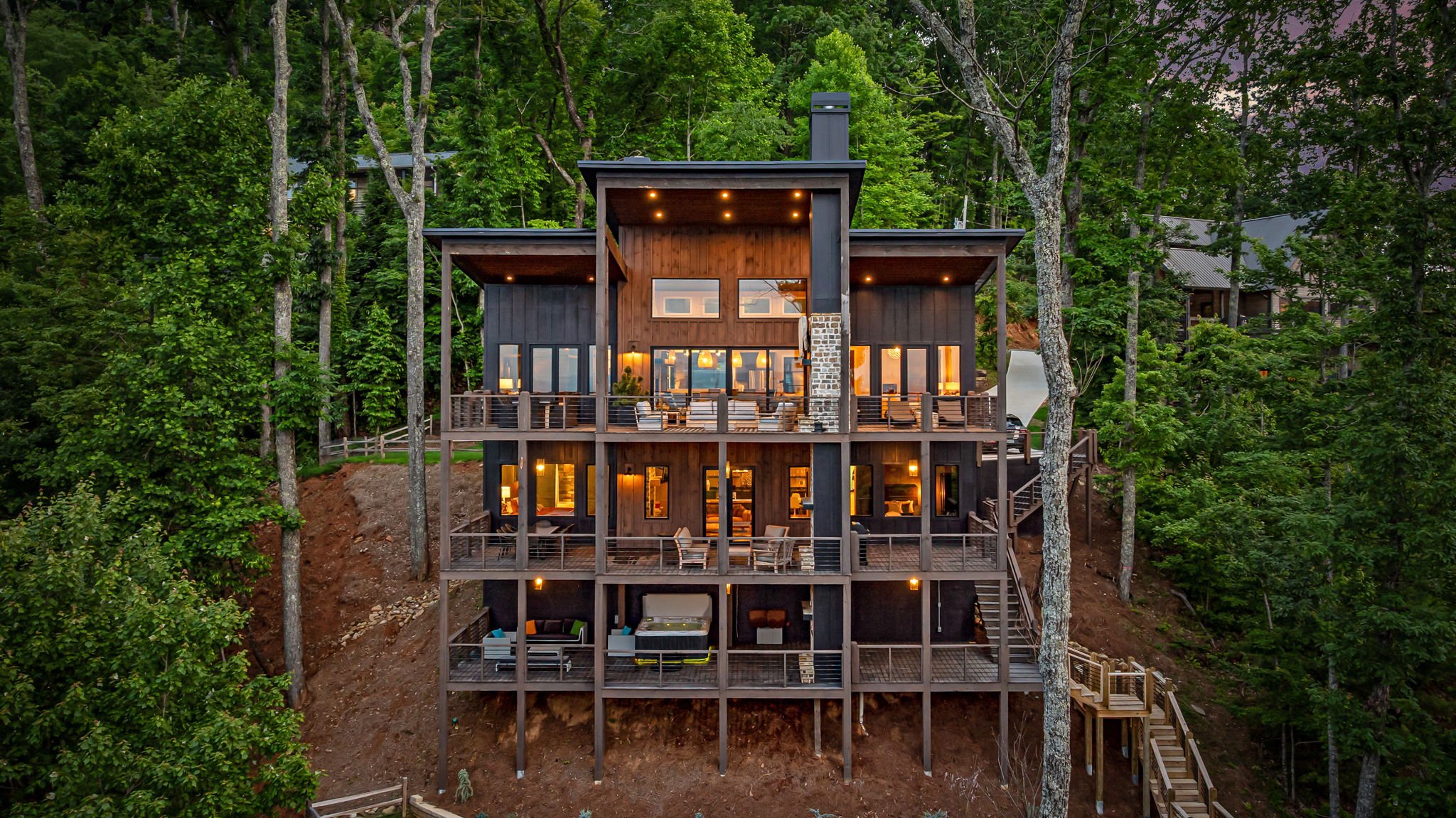 Admire this stunning modern mountain retreat featuring multi-level decks, panoramic mountain & lake views, outdoor lounge areas, floor-to-ceiling windows, & striking architectural design—an elevated luxury escape surrounded by serene forest scenery.