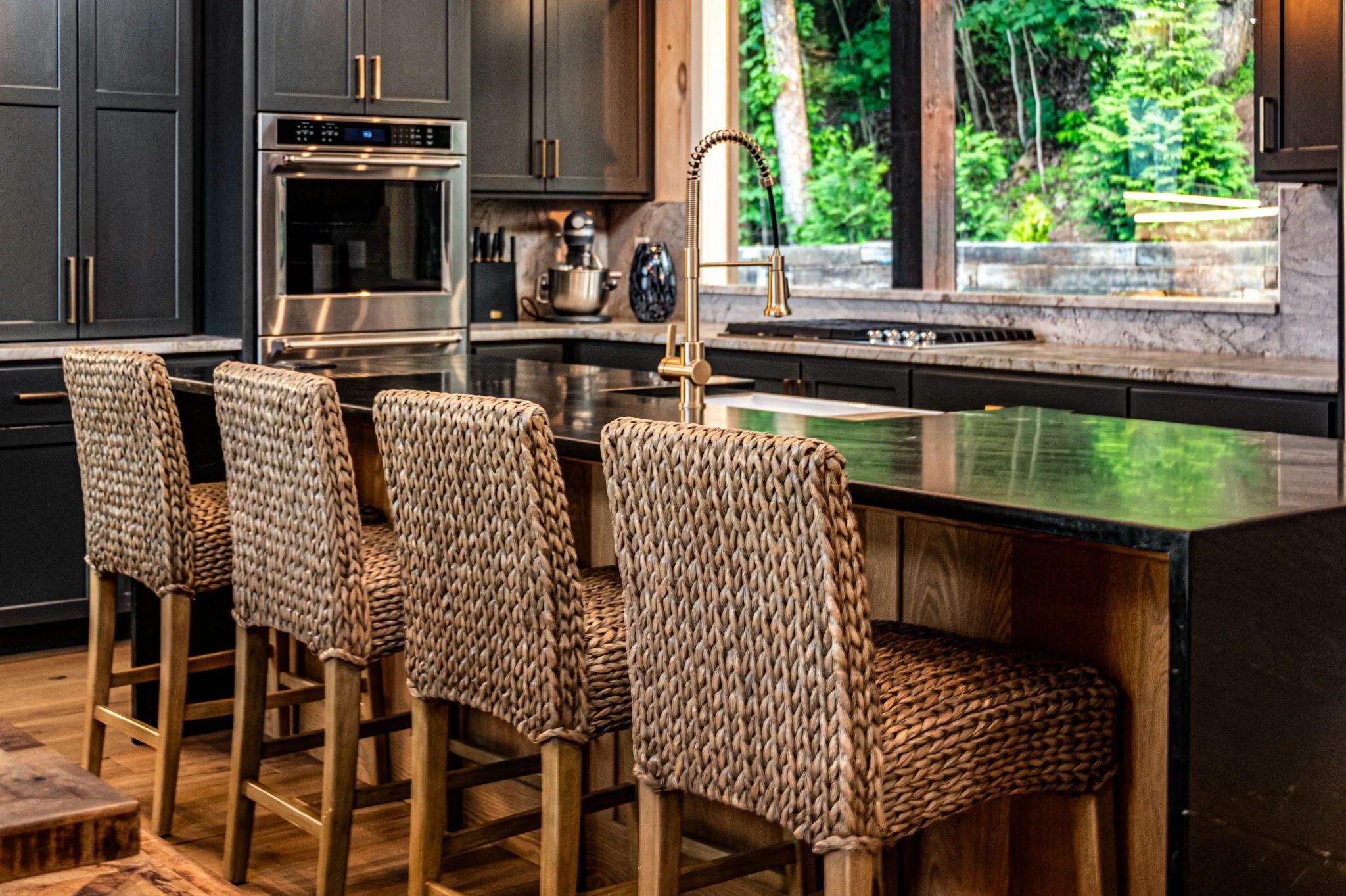 Gather at the expansive island with woven bar seating, sleek countertops, and a designer faucet. Premium appliances, custom cabinetry, and natural light from large windows create an elegant space for cooking, cocktails, and conversation.