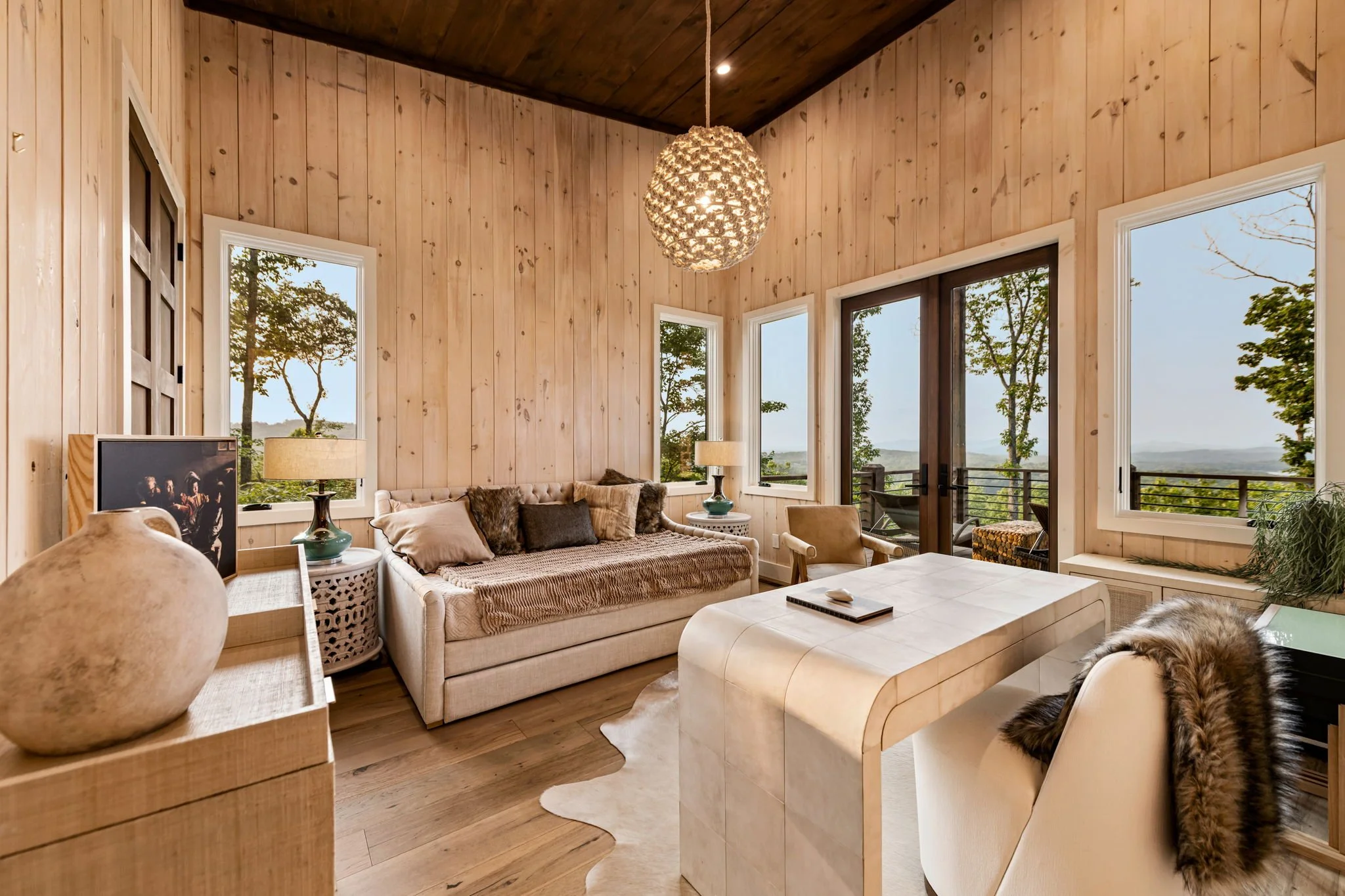 Unwind in Bedroom 2, a beautifully designed retreat featuring plush seating, designer lighting, and expansive windows framing stunning mountain and lake views. Private terrace access and refined furnishings create a serene space to relax & recharge.