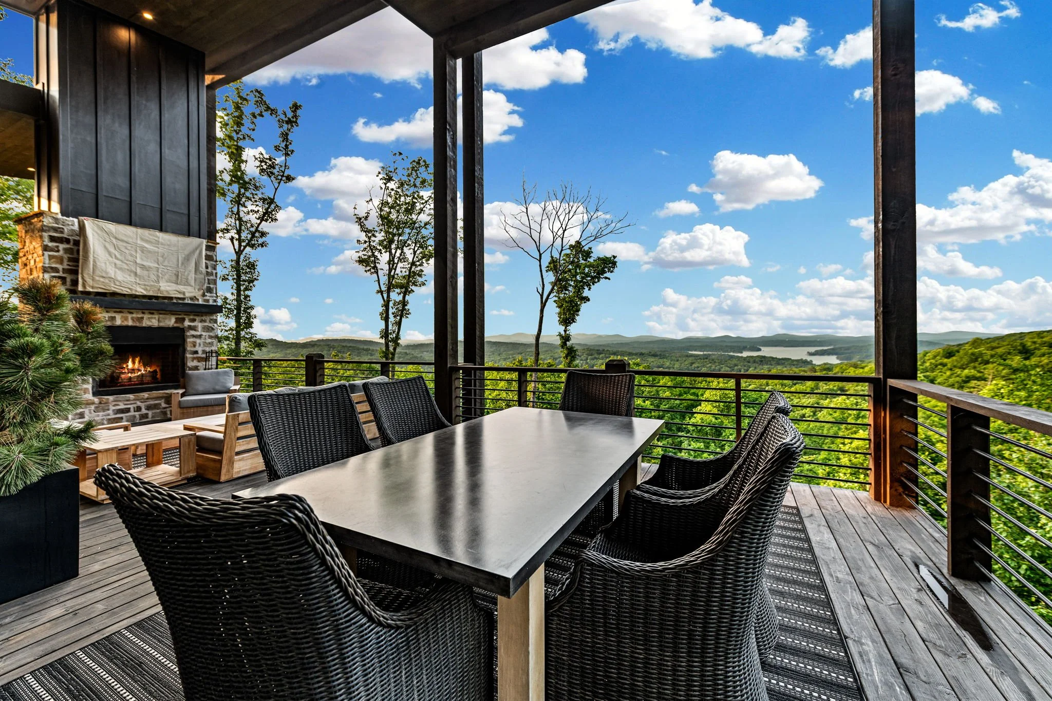 Dine outdoors on the covered deck featuring a spacious dining table, comfortable seating, outdoor fireplace nearby, and sweeping mountain & lake views—the perfect setting for unforgettable meals surrounded by breathtaking scenery.