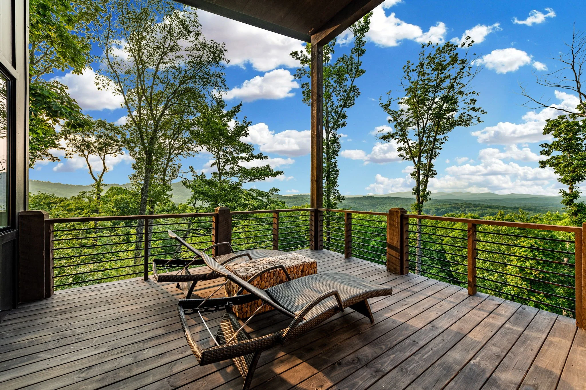 Lounge on the expansive covered deck featuring comfortable chaise loungers and breathtaking panoramic mountain & lake views—a peaceful luxury spot perfect for sunbathing, morning coffee, or relaxing in the fresh mountain air.