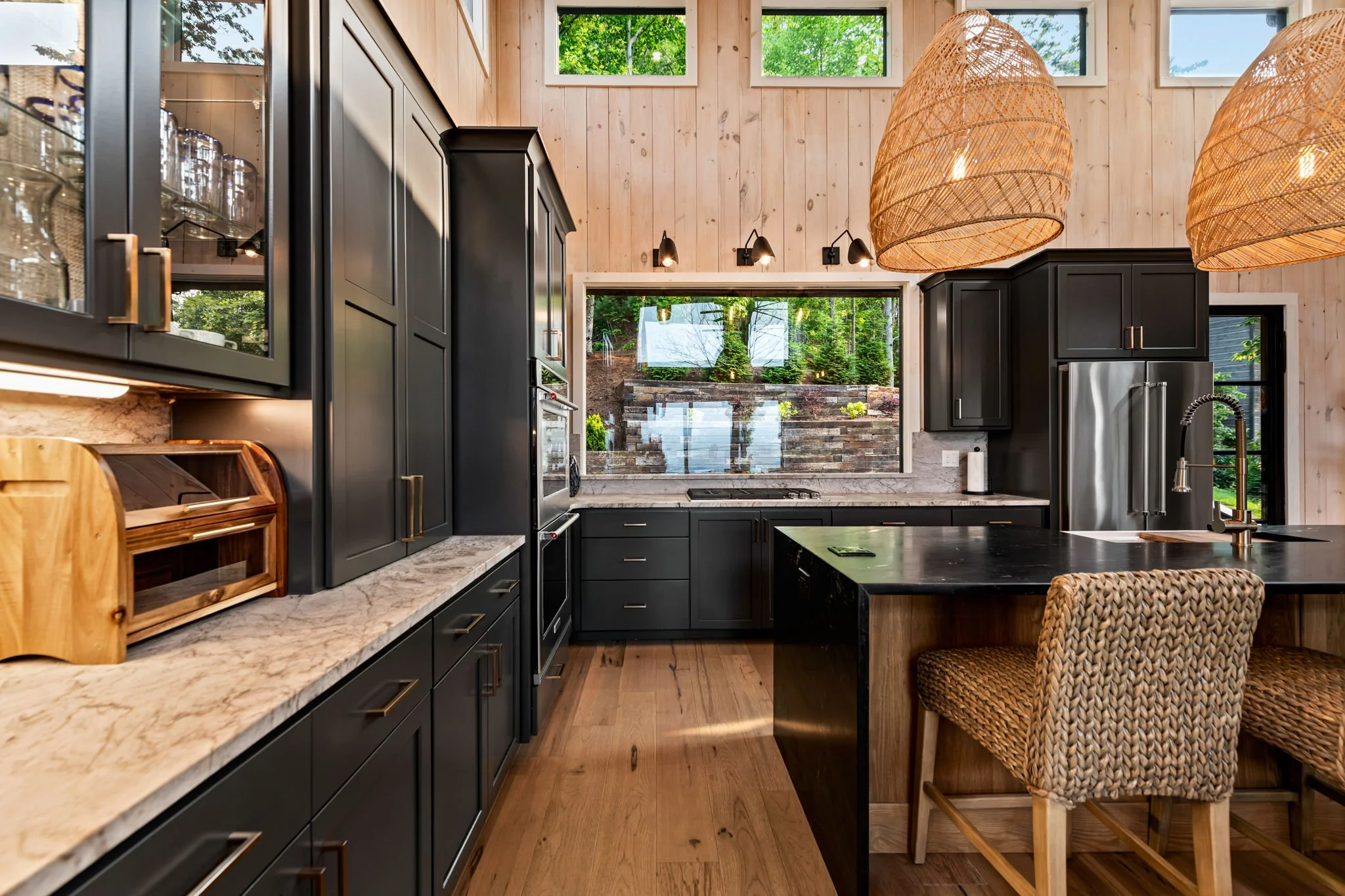 Prepare meals in this luxury chef’s kitchen featuring custom cabinetry, quartz countertops, large island with seating, stainless steel appliances, double ovens, designer pendant lighting, & oversized windows bringing in natural light & forest views.