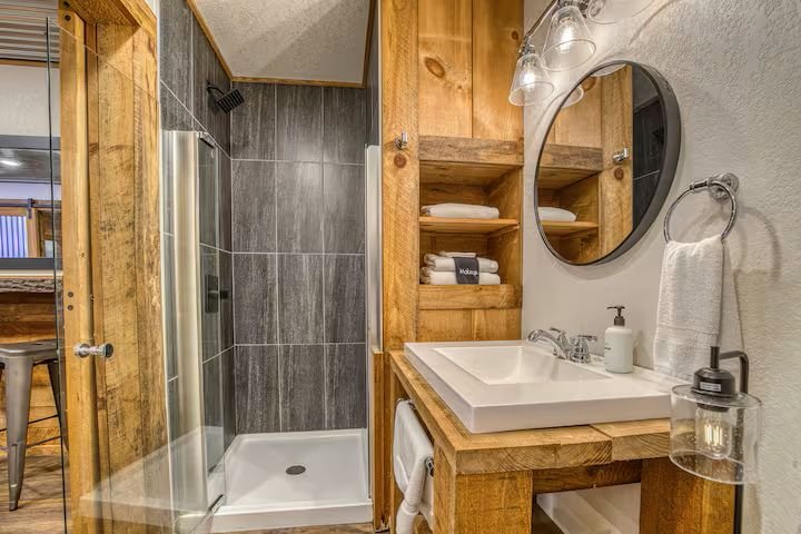 The downstairs bathroom features a sleek, modern design with a tiled walk-in shower, rustic vanity, and stylish finishes. Stocked with shampoo, conditioner, body wash, soaps, and plenty of fresh towels to keep everyone refreshed during their stay.