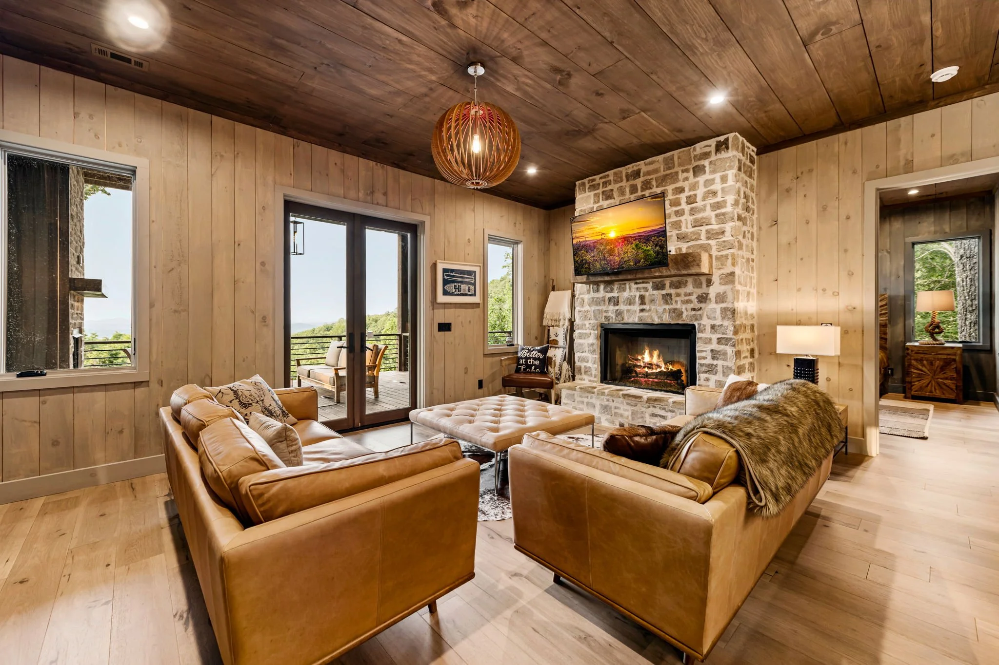 Relax in this cozy lounge featuring plush leather sofas, Smart TV, a floor-to-ceiling stone fireplace, designer lighting, and deck access—a warm and inviting space perfect for movie nights, conversation, and unwinding after a day of adventure.
