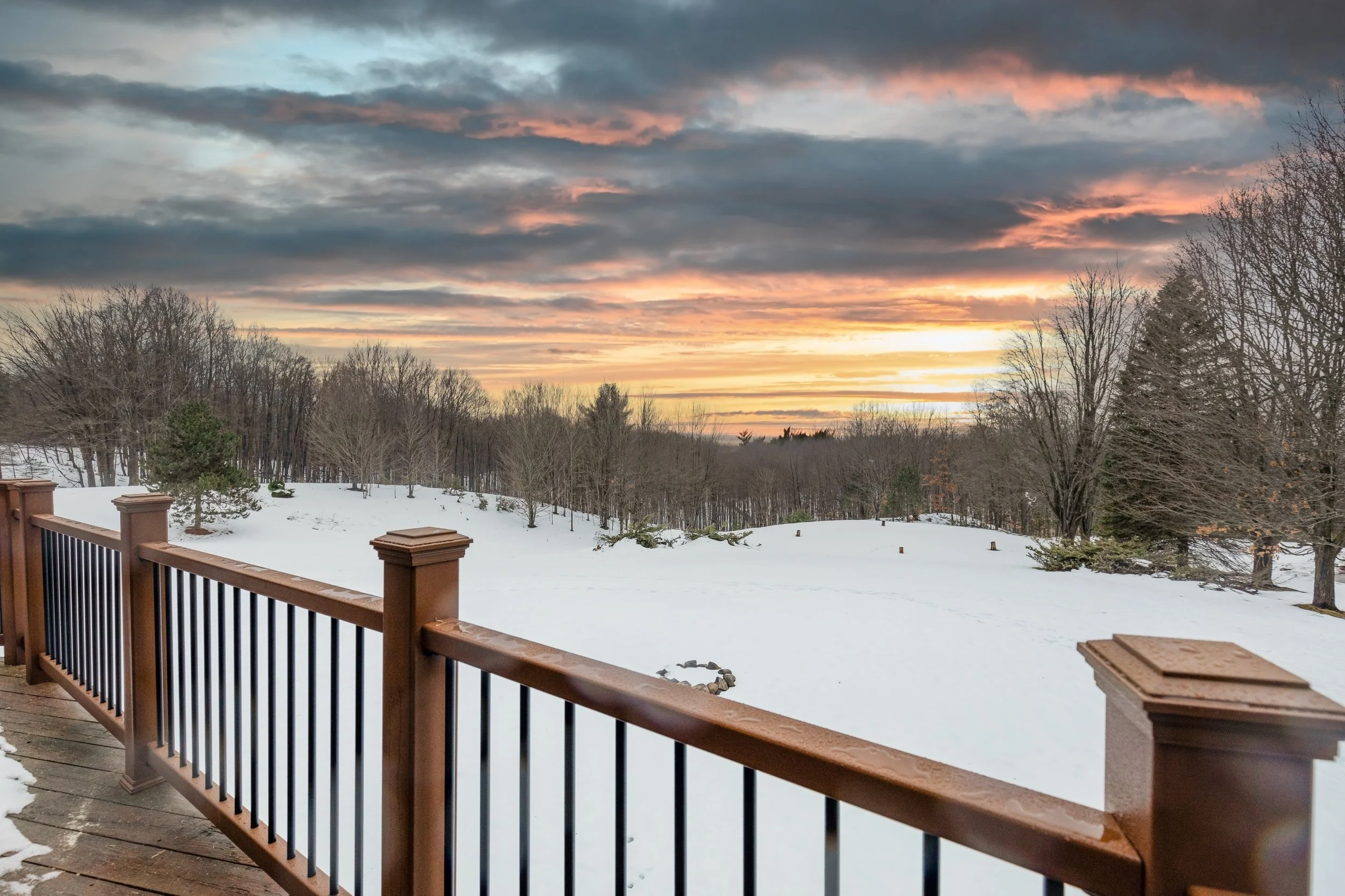 A spacious covered deck overlooking a peaceful winter landscape, where fresh snow blankets the ground and bare trees frame the view. Enjoy crisp mountain air, quiet surroundings, and the comfort of a sheltered outdoor space—perfect for morning coffee