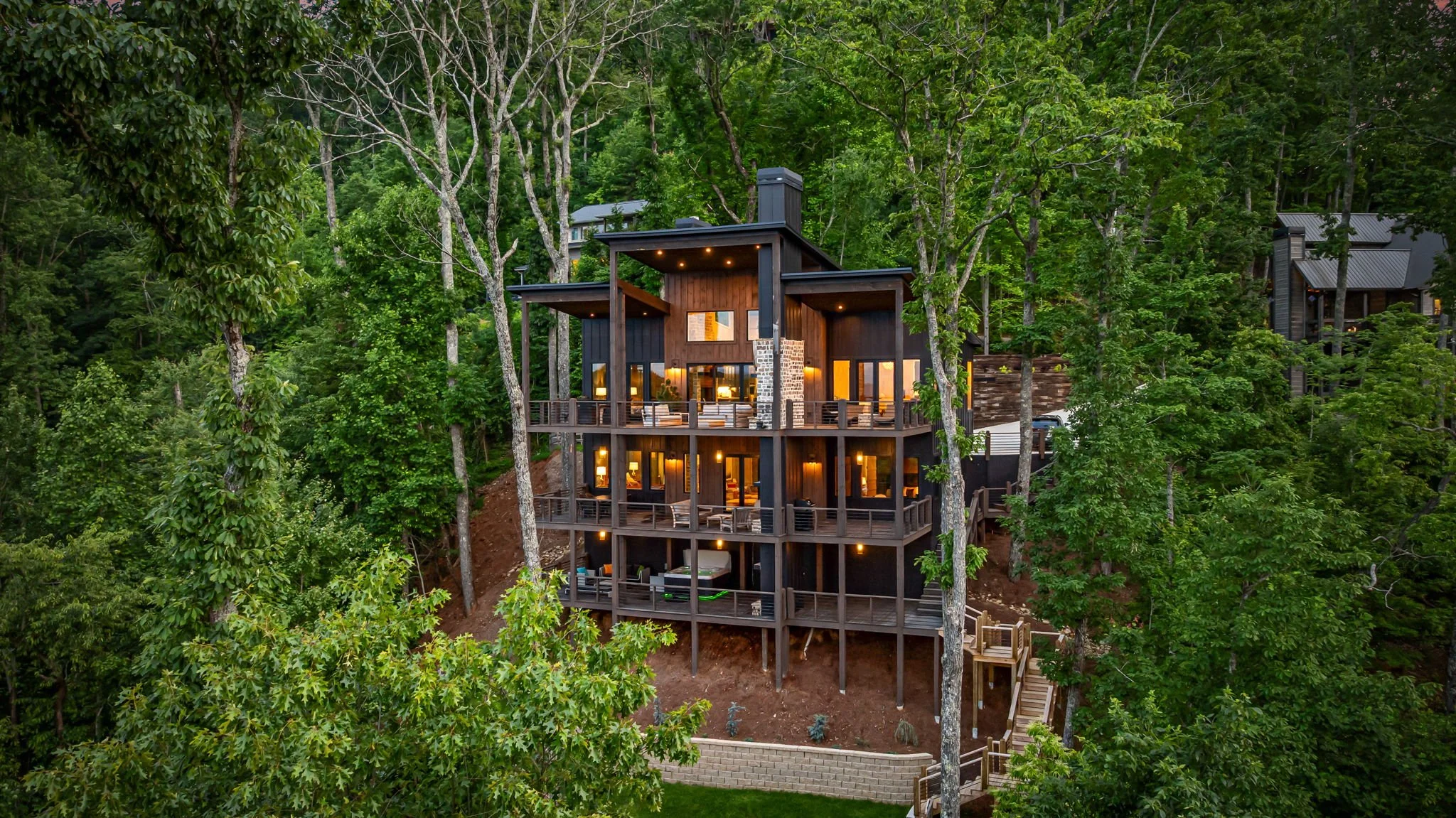 Admire this stunning modern mountain retreat featuring multi-level decks, panoramic mountain & lake views, outdoor lounge areas, floor-to-ceiling windows, & striking architectural design—an elevated luxury escape surrounded by serene forest scenery.