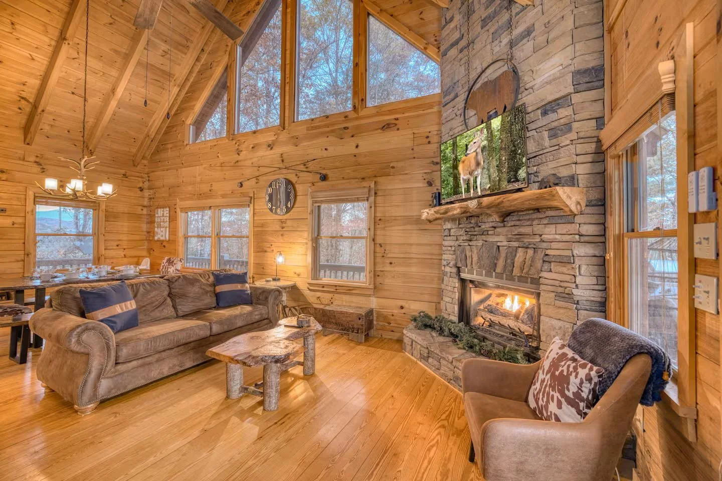 The main-level great room features tall ceilings, a modern cabin feel, large gas fireplace, a big-screen TV, and plenty of seating. This open-concept layout creates the perfect family-friendly space for gathering, relaxing, and entertaining together.