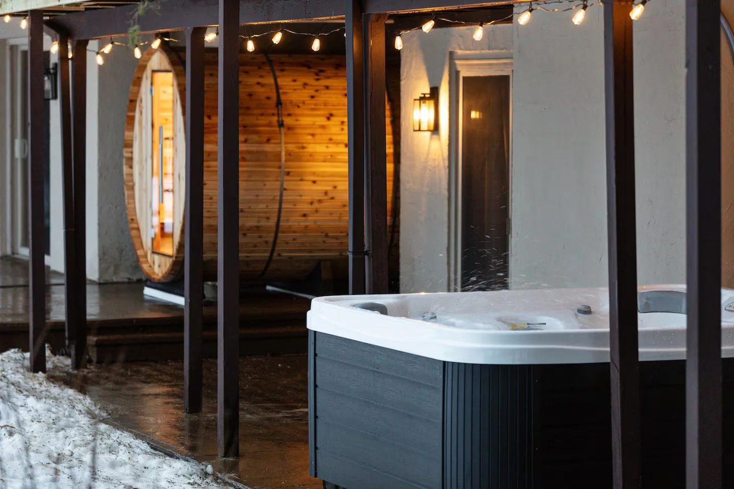 The back patio features a covered 7-person jacuzzi + 6-person barrel sauna, both tucked under the deck. String lights add ambiance, while both offer stunning sunset views over the valley, they’re perfect after a long day of ski or golf at the resort!