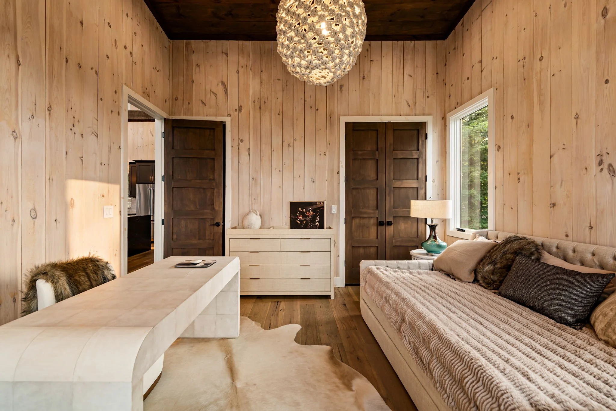 Relax in this elegant bedroom featuring a plush daybed, designer lighting, warm wood walls, and refined furnishings. Thoughtfully styled with serene tones and natural light, it offers a peaceful retreat within this elevated mountain getaway.