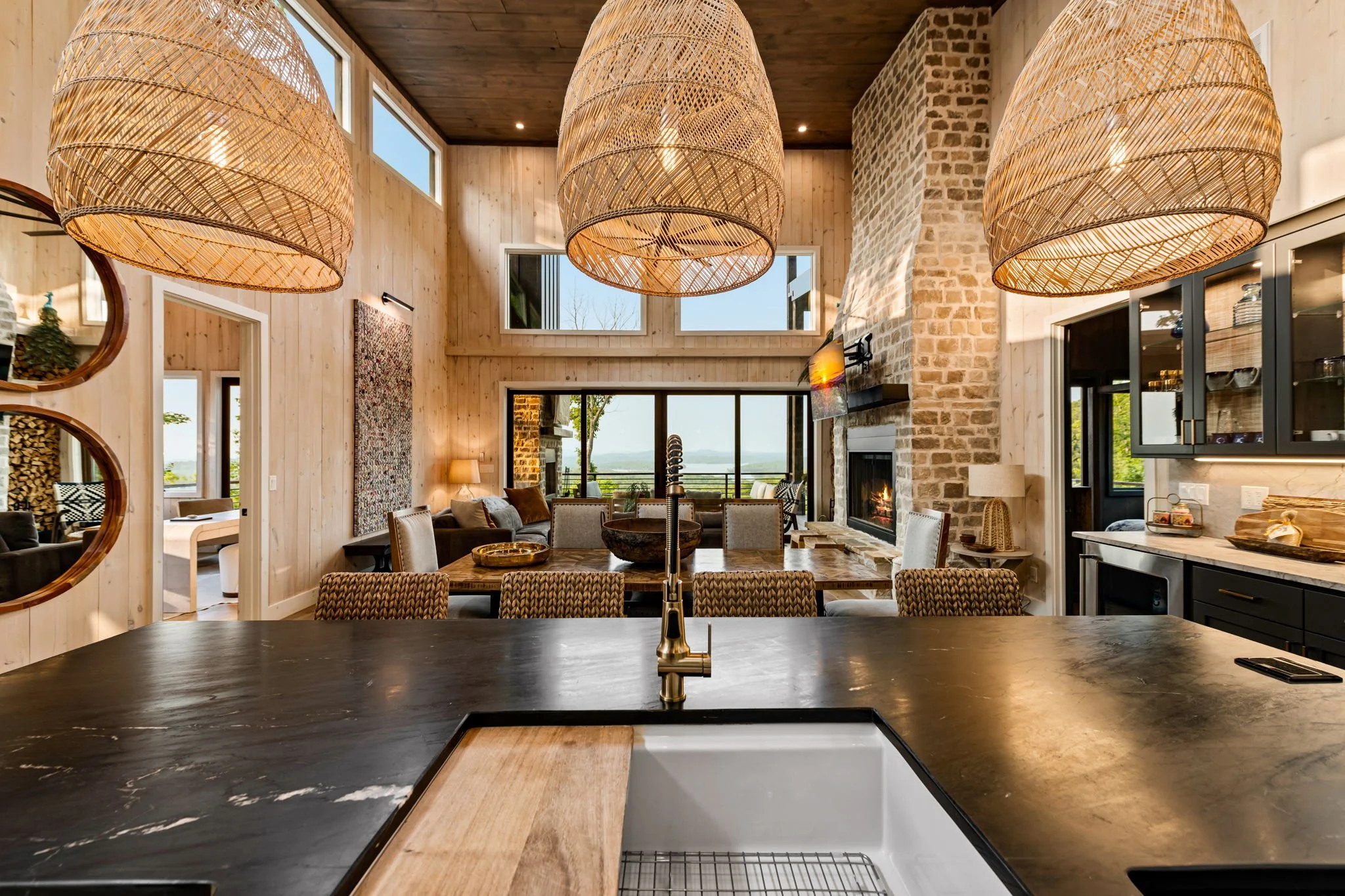 Entertain in this stunning open-concept space featuring a chef’s kitchen with large island, prep sink, stainless appliances, designer pendant lighting, dining area, floor-to-ceiling stone fireplace, and panoramic mountain views—perfect for gathering.