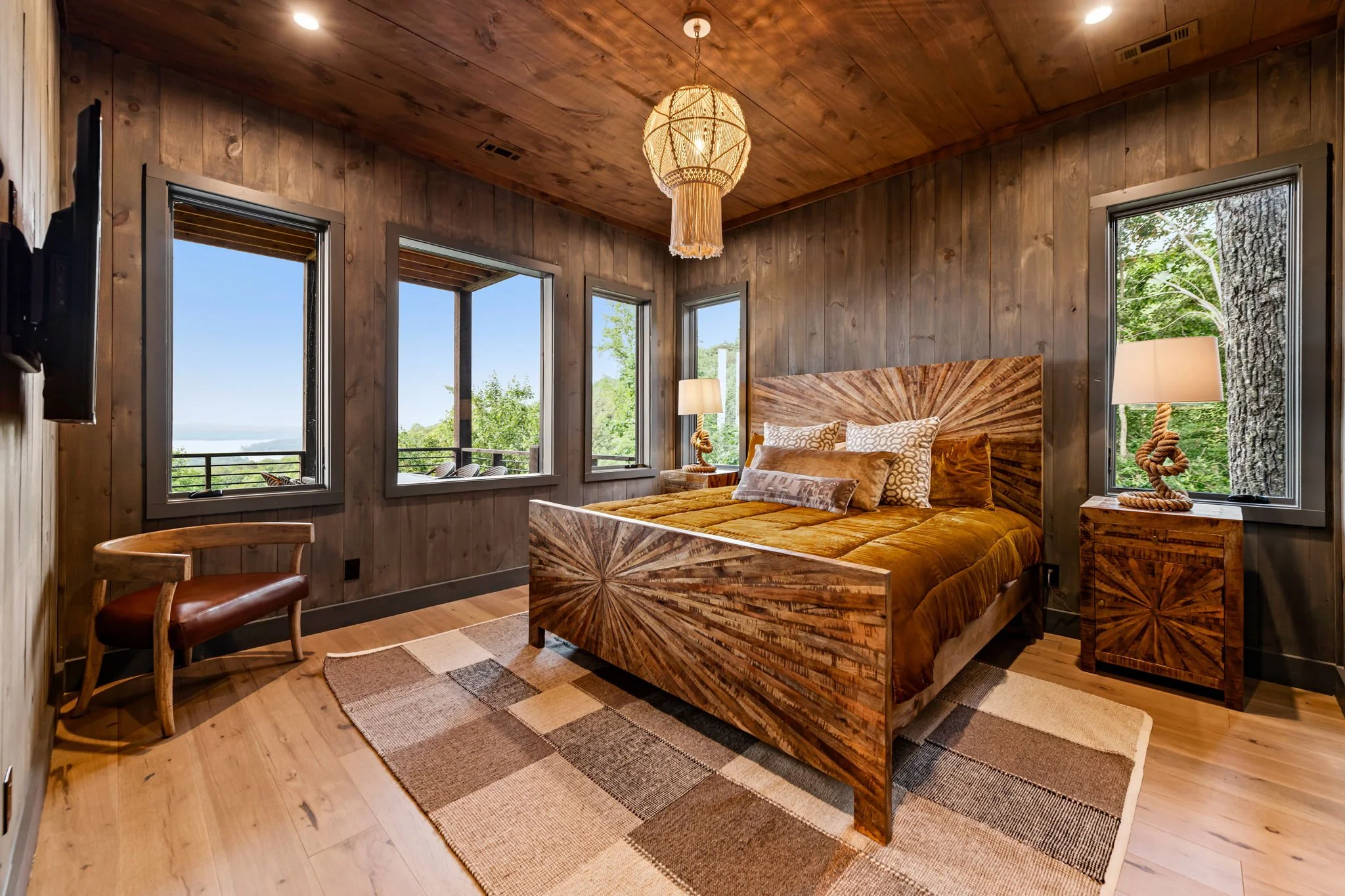 Unwind in Bedroom 4 featuring a stunning handcrafted wood bed, plush bedding, designer chandelier, and expansive windows that invite natural light and peaceful mountain views—creating a warm, refined retreat for restful nights in luxury comfort.