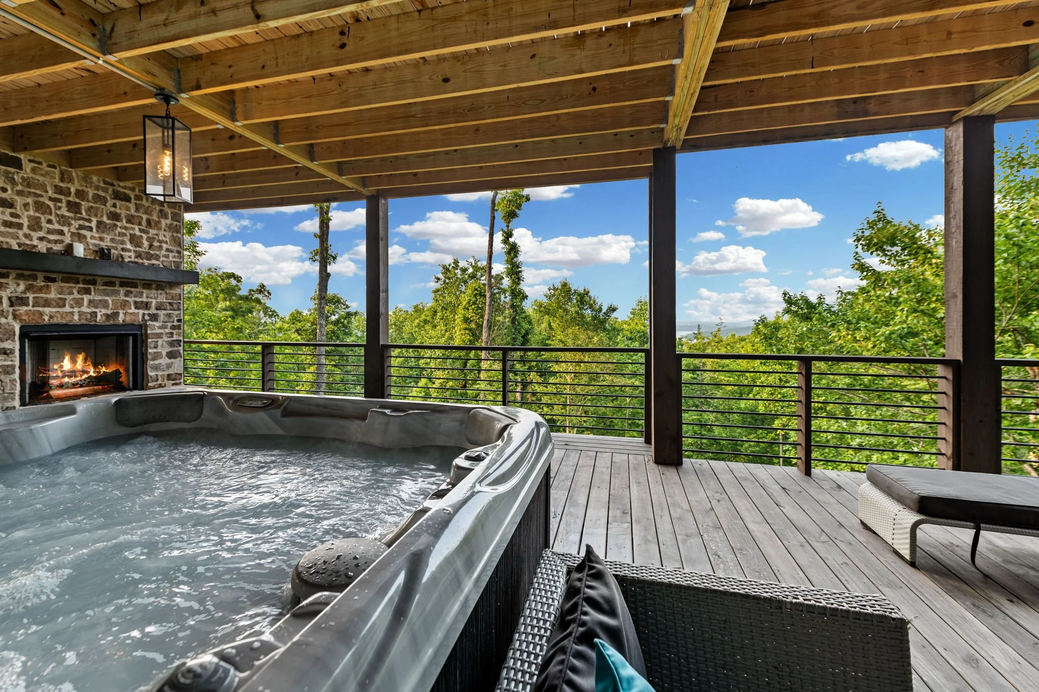 Unwind in the private outdoor hot tub on a covered deck featuring a stone fireplace, lounge seating, and sweeping mountain views. A luxurious open-air retreat perfect for relaxing soaks and cozy evenings surrounded by nature.