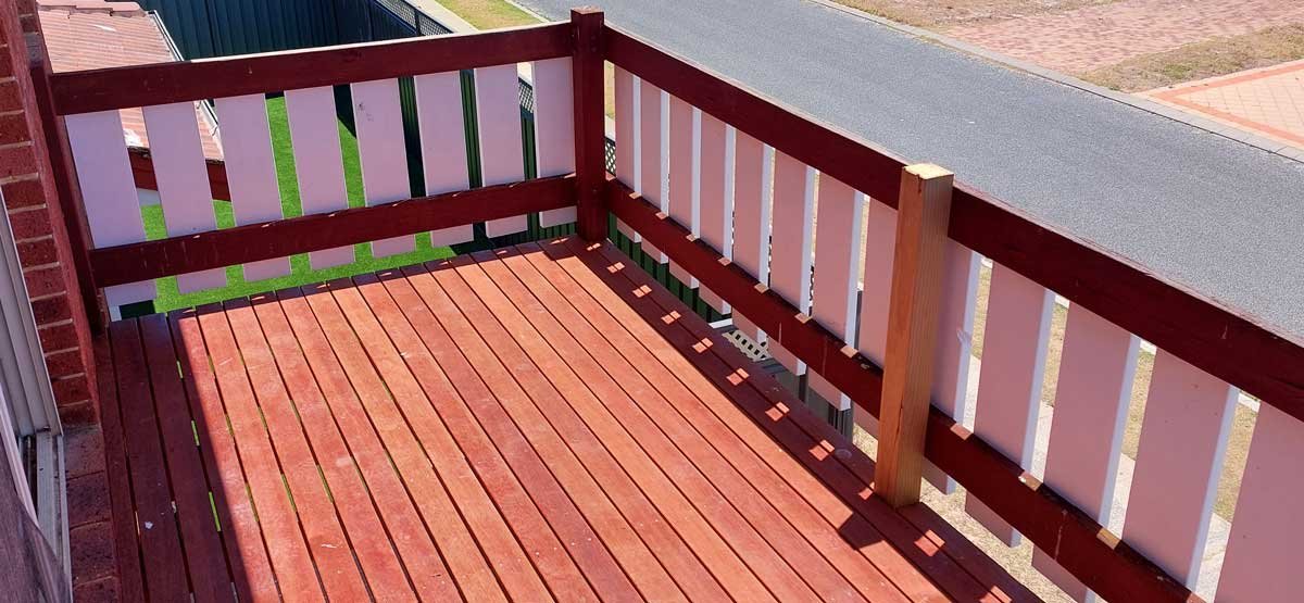 View of a wooden balcony with Jarrah decking and a matching railing, overlooking a residential street and neighboring yards.