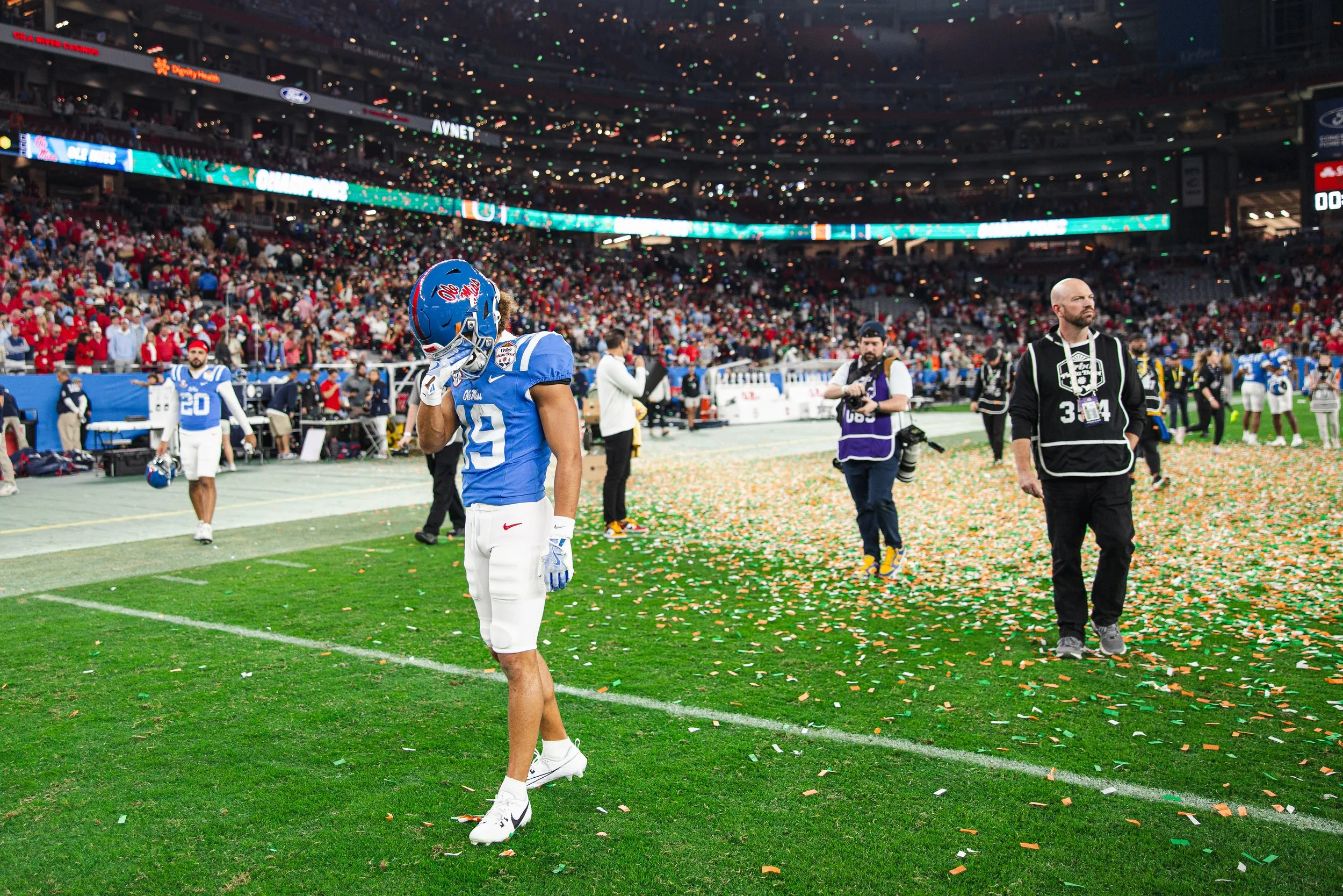 Cayden Lee in blue jersey and white pants standing on a football field surrounded by colorful confetti, with a stadium filled with spectators in the background.