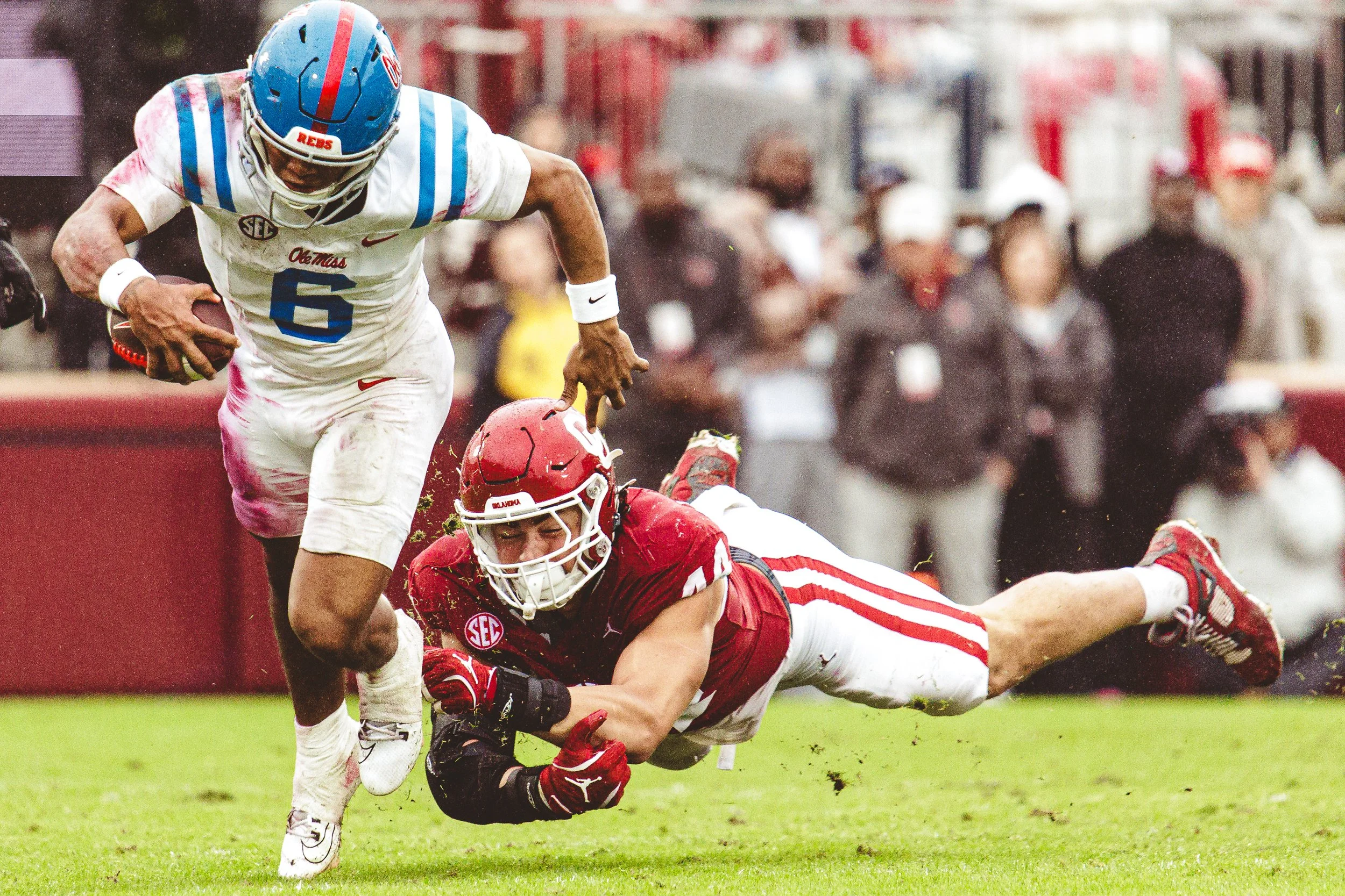Trinidad Chambliss from the University of Mississippi running while clutching the football, and a player in a red uniform from the University of Oklahoma diving to tackle him.