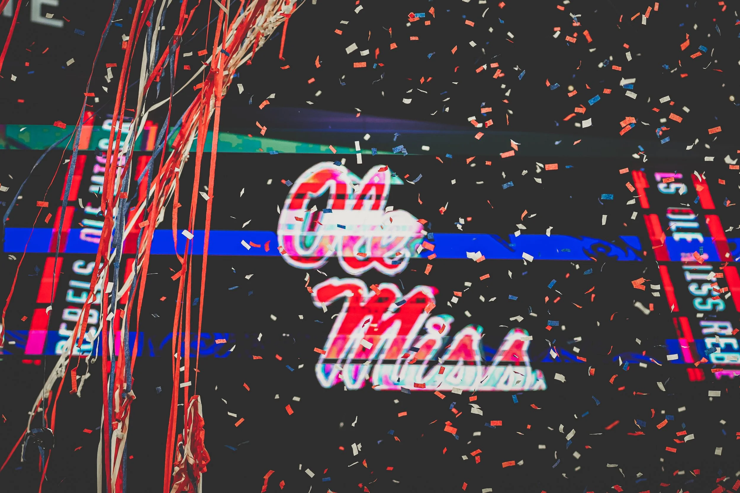 Colorful neon sign reading 'Ole Miss' with falling confetti and streamers around it, celebrating.