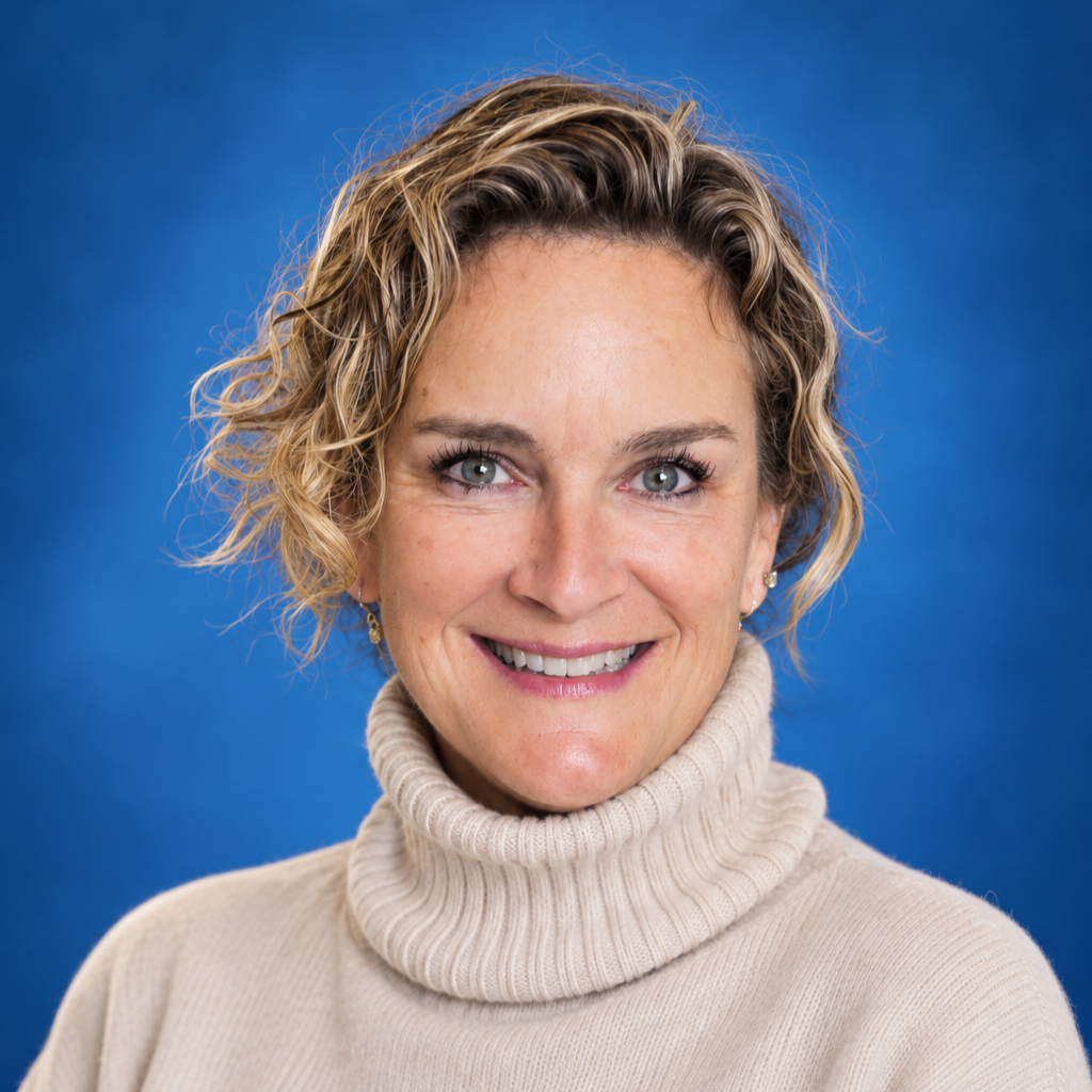 A woman with curly blonde hair and blue eyes smiling, wearing a beige turtleneck sweater against a blue background.