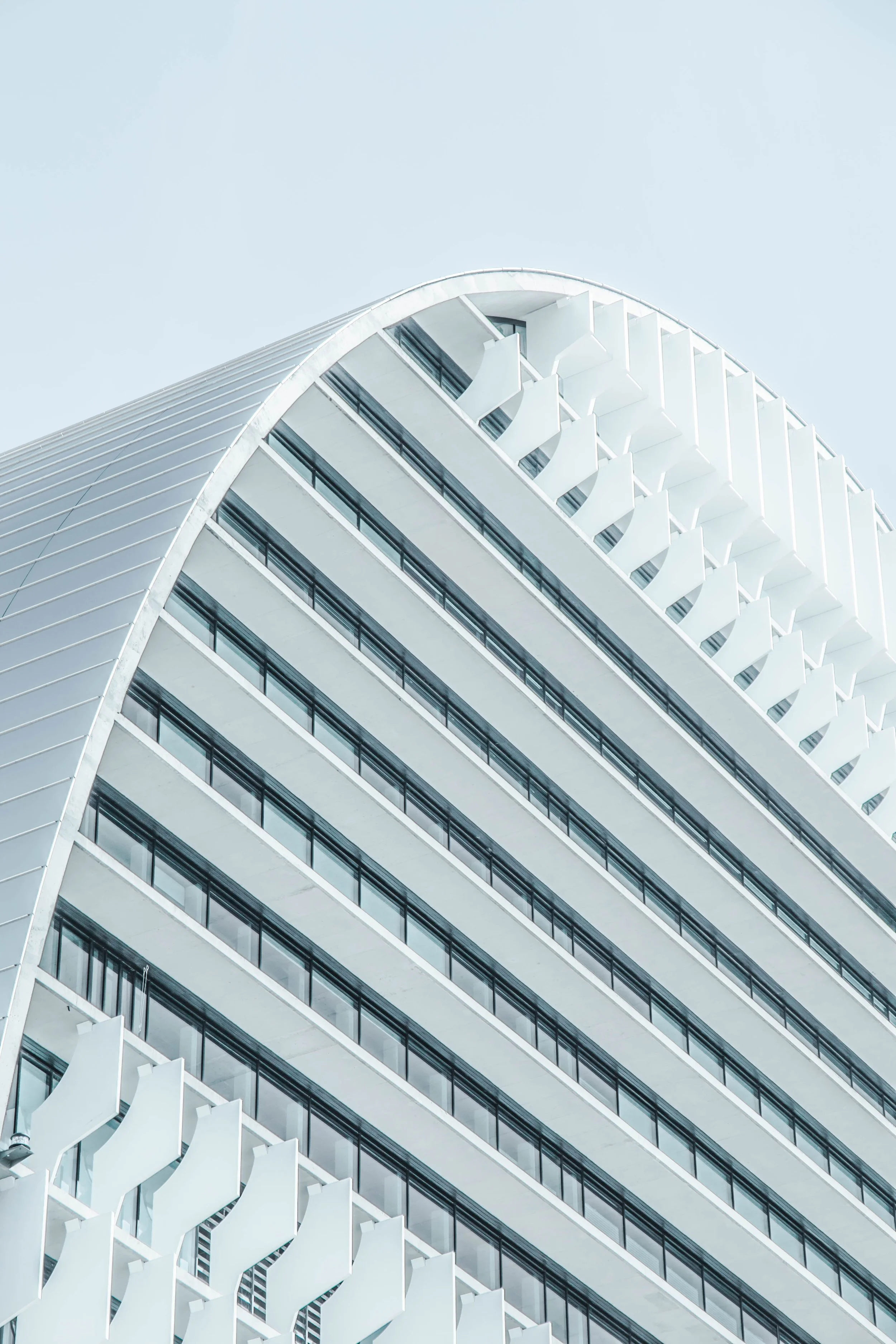 Close-up of a modern, white architectural building with multiple floors, balconies, and angular design elements, against a pale sky.