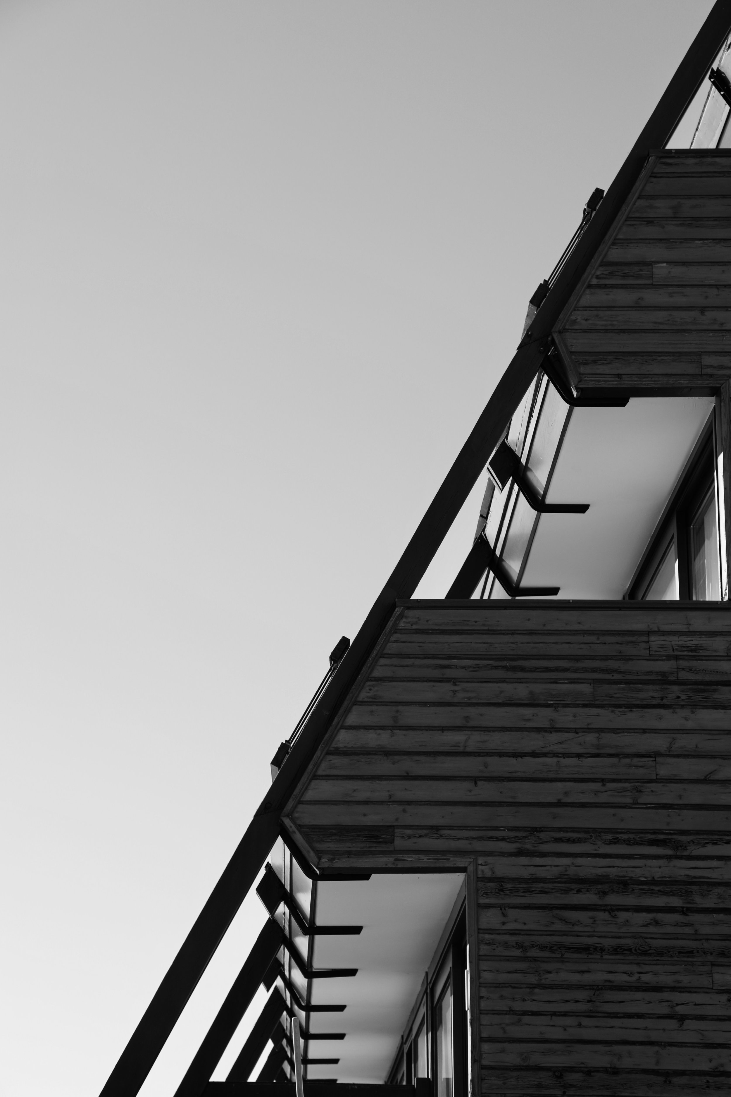 Vue en contre-plongée d'un bâtiment moderne en bois avec une structure inclinée et des fenêtres, ciel clair.