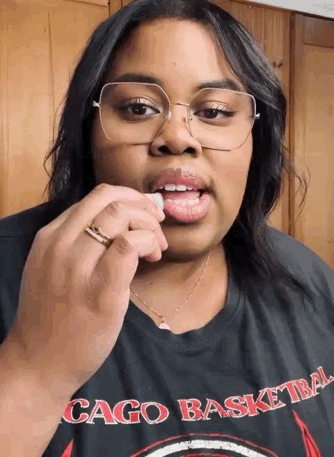 Woman with glasses and dark hair touching her lips, wearing a black T-shirt that says 'CAGO BASKETBALL' in red and white letters.