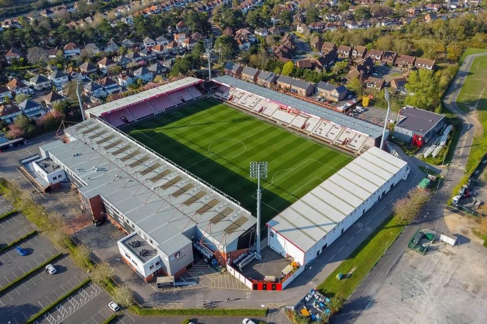 Aerial view of a football stadium with a lush green field, surrounded by four stands.
