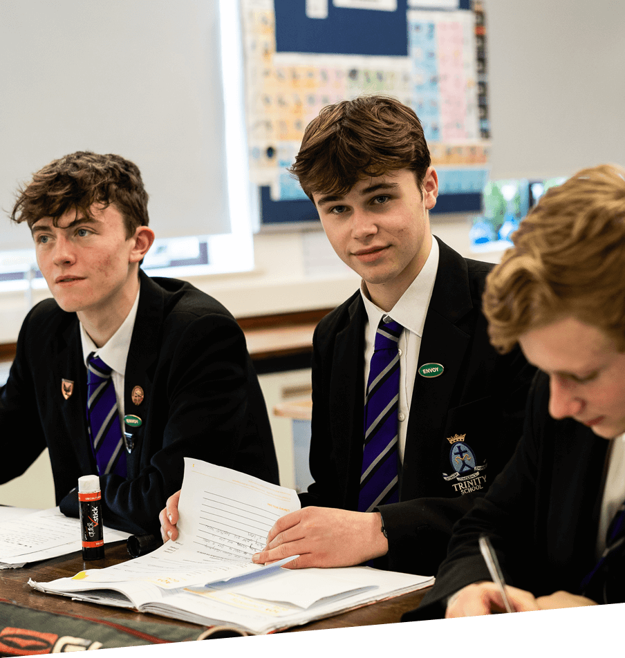 Three young men of Trinity School sitting at a table in school uniforms, involved in an academic discussion.