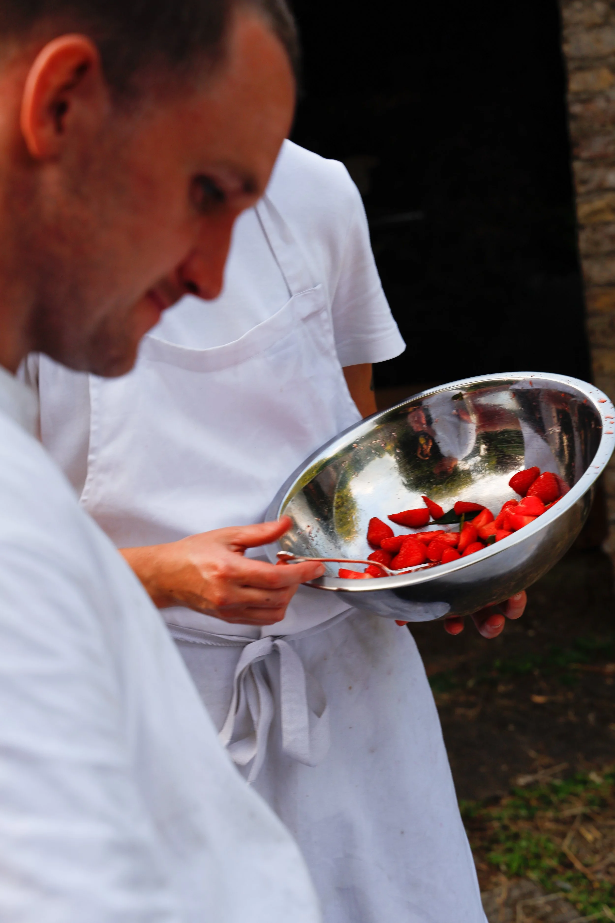 Person holding a metal bowl of strawberries.