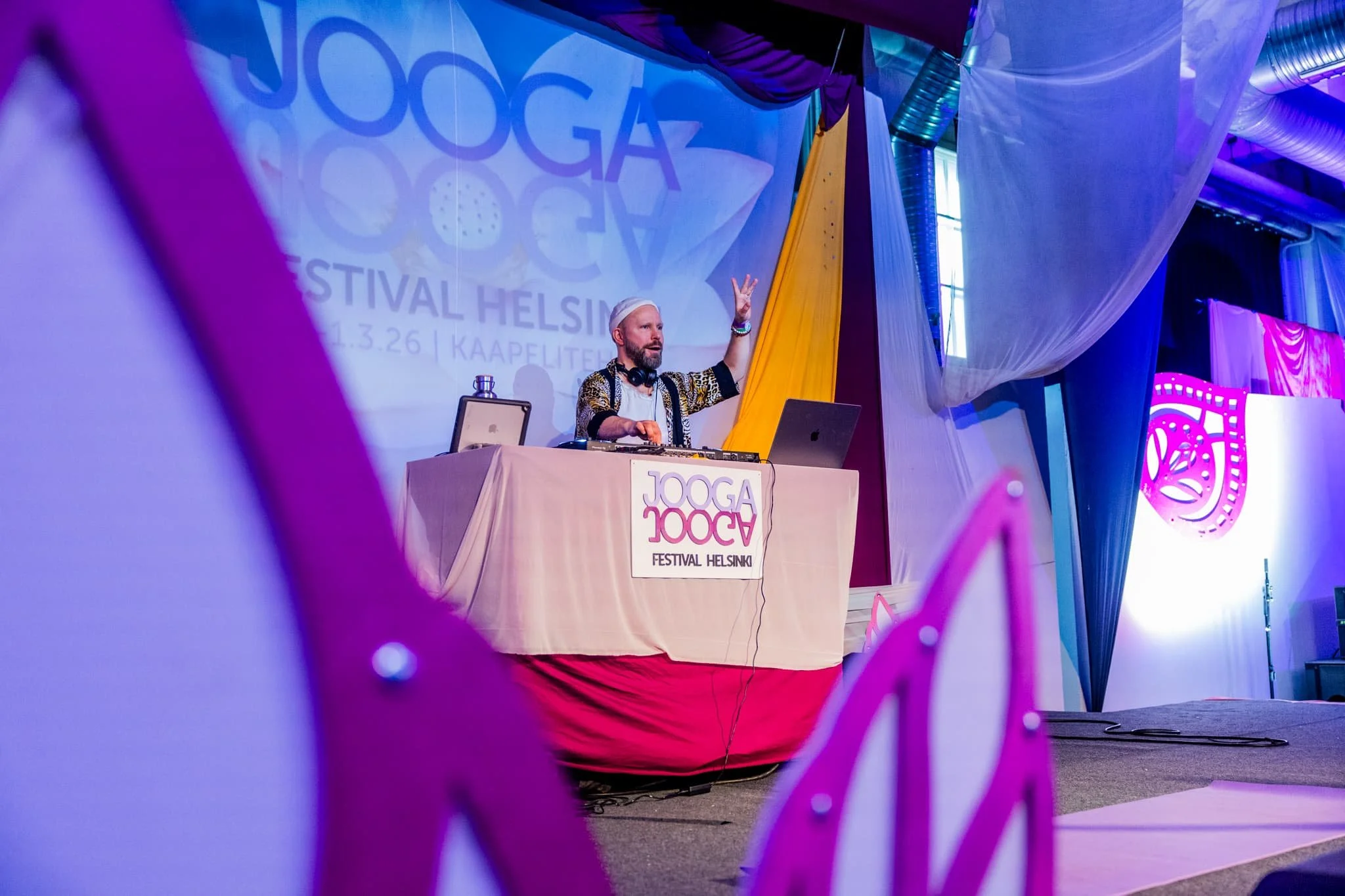 Esiintyjä lavalla Joogafestivalin logon edessä violetissa valaistuksessa