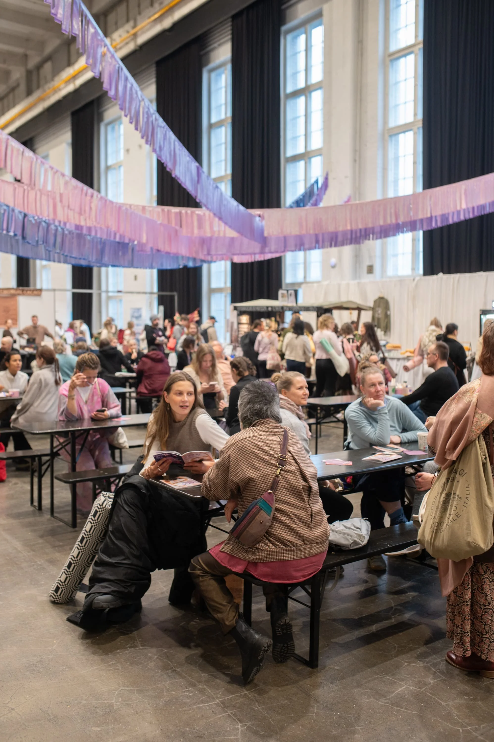 Festivaalivieraita istumassa ja juttelemassa Merikaapelihallin kahvila-alueella värikkäiden kattokoristeiden alla