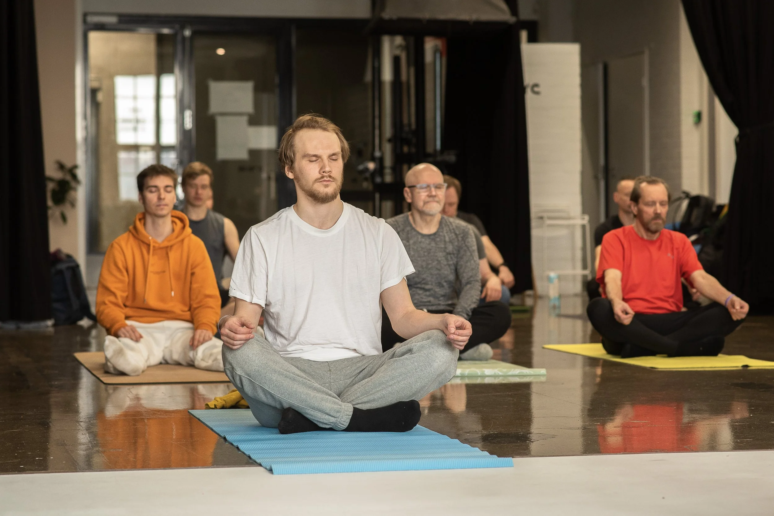Miehiä istumassa meditaatiossa joogatunnilla
